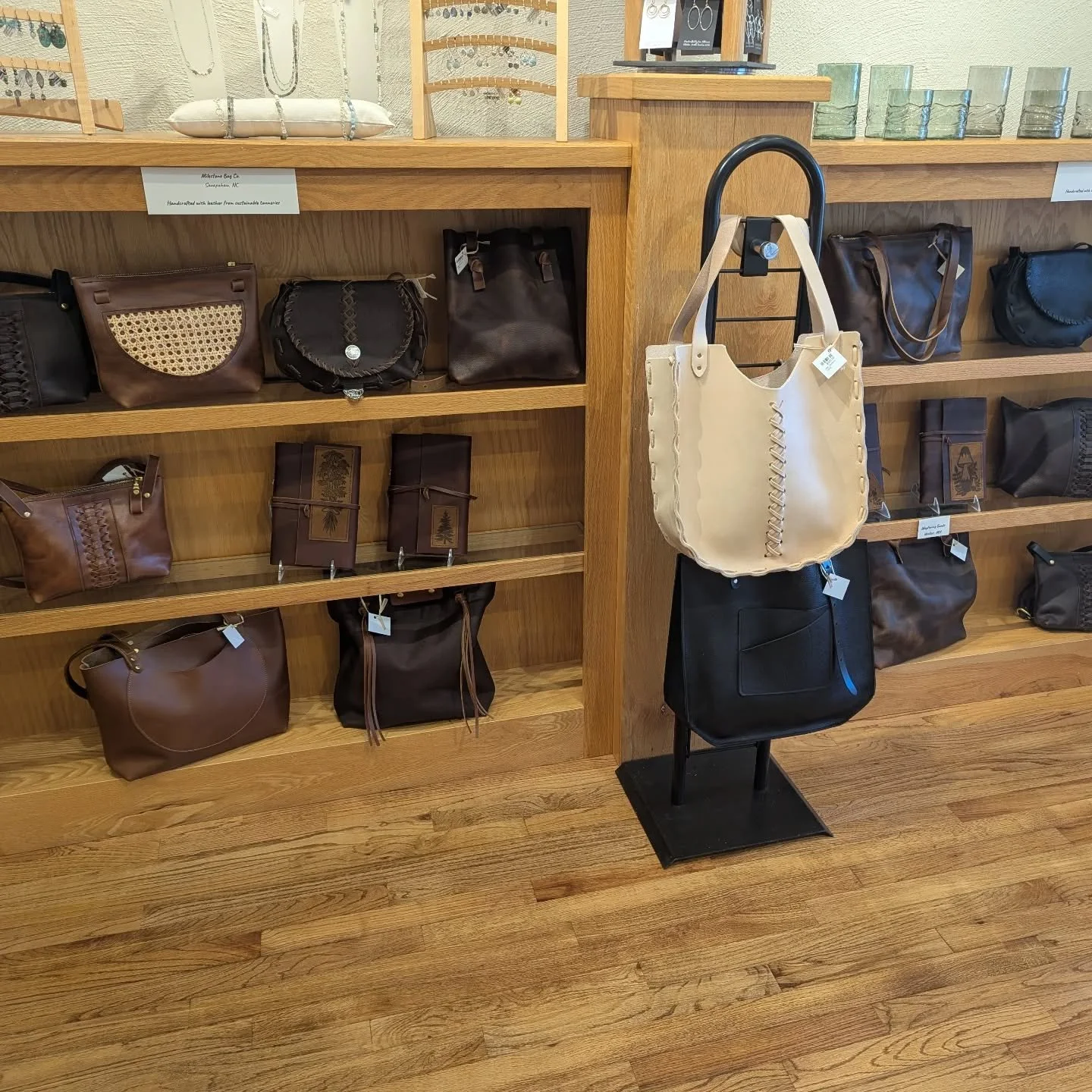 Display of leather handbags, wallets, and jewelry on wooden shelves and a stand, in a retail store.