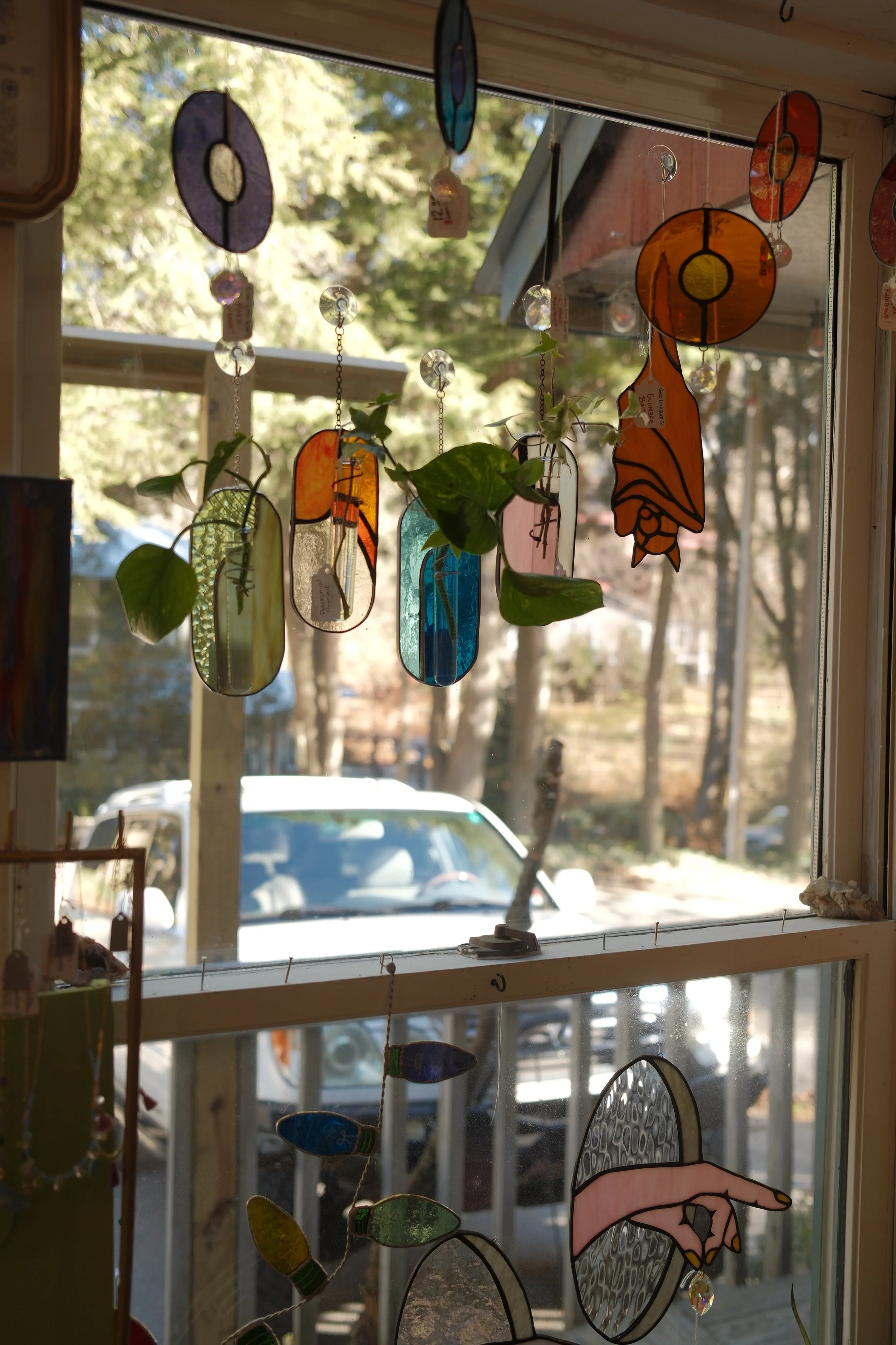Decorative stained glass sun catchers hanging in a window with garden and trees visible outside.