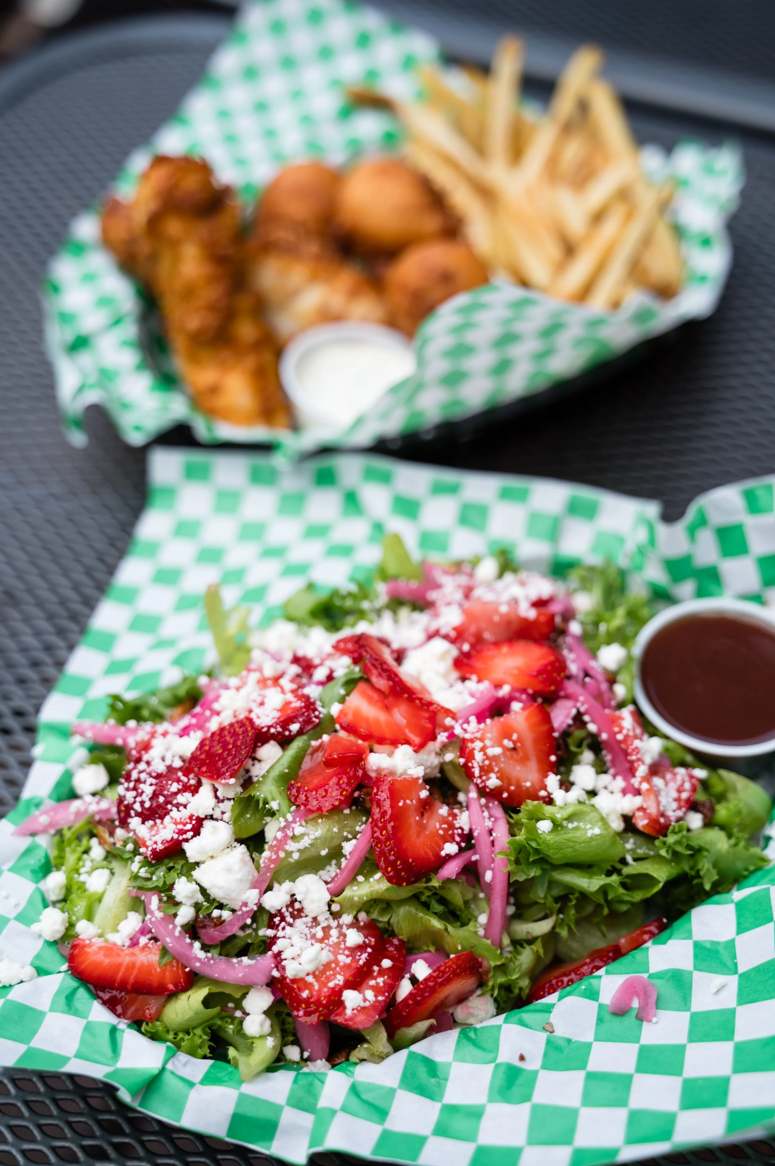 Colorful salad with strawberries, feta cheese, and pink onions served on a green and white checkered paper in a basket.