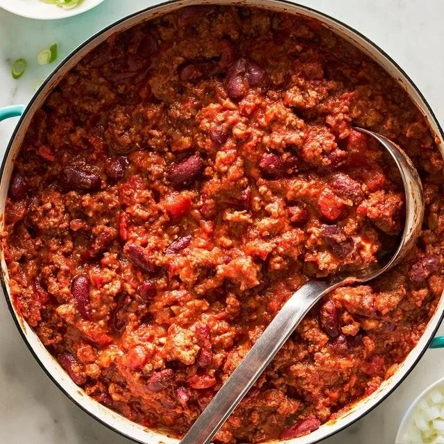 Pot of cooked chili with ground beef, beans, and tomato sauce, with a metal spoon inside.