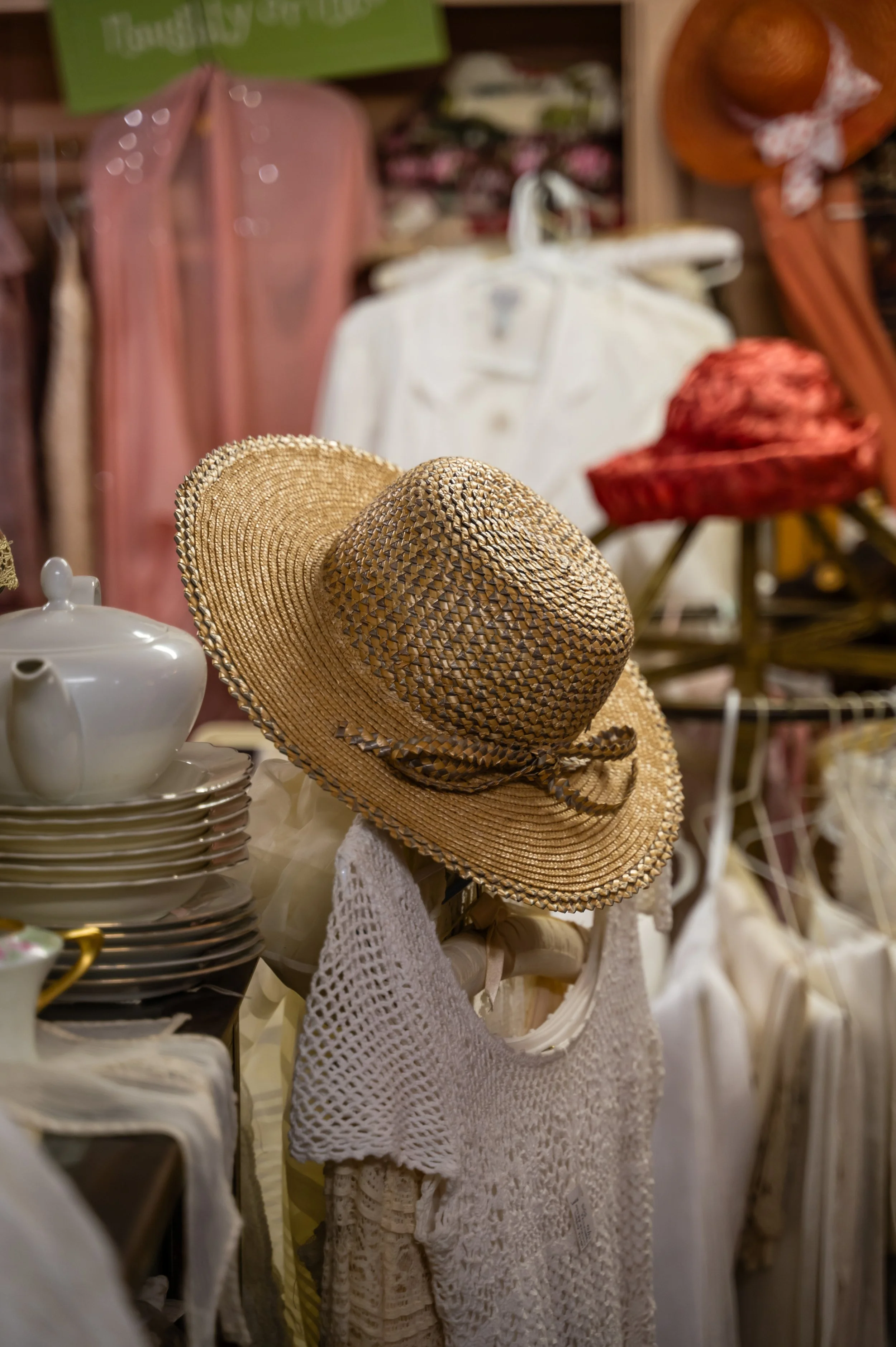 A straw hat is displayed on a mannequin in a store with various clothing and accessories in the background.