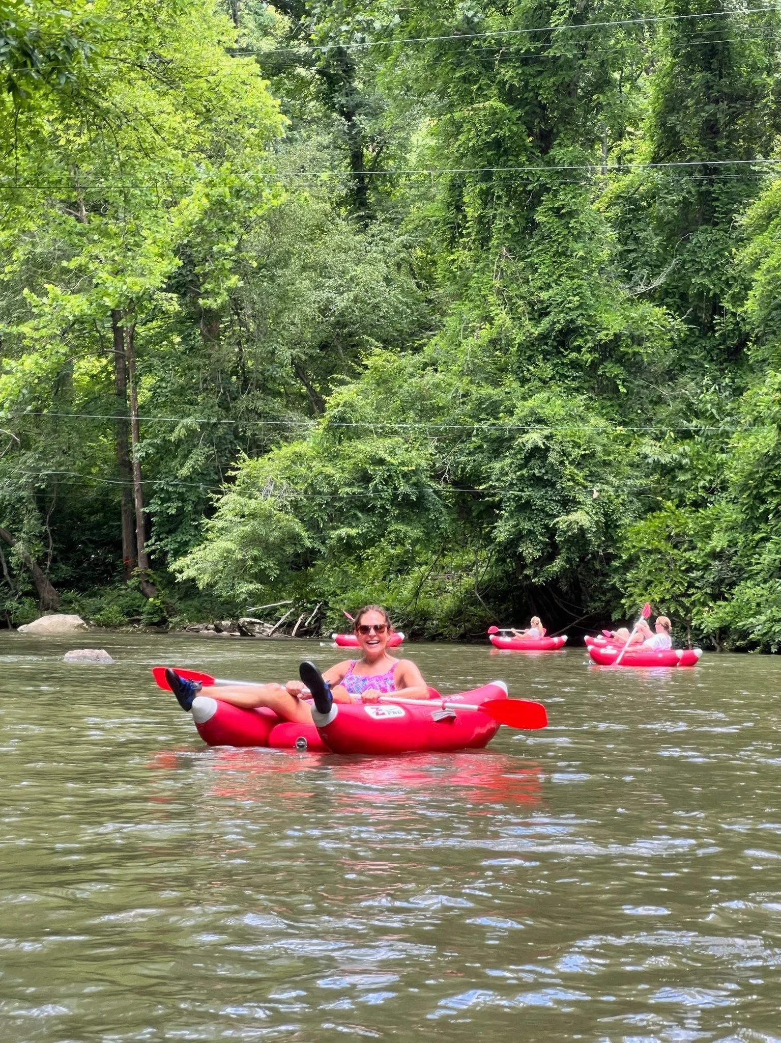 People kayaking on a river surrounded by dense green trees.