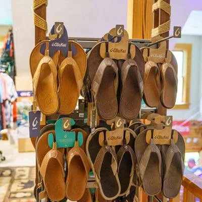 Display of various leather slippers in different shades of brown and tan hanging on a wooden rack in a retail store.