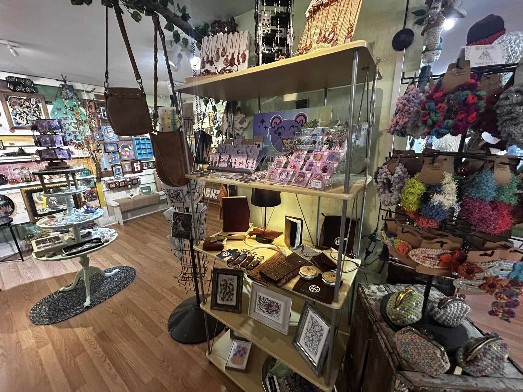 A cozy boutique with various handmade and vintage items displayed on shelves and tables, including jewelry, framed art, and knitted accessories.