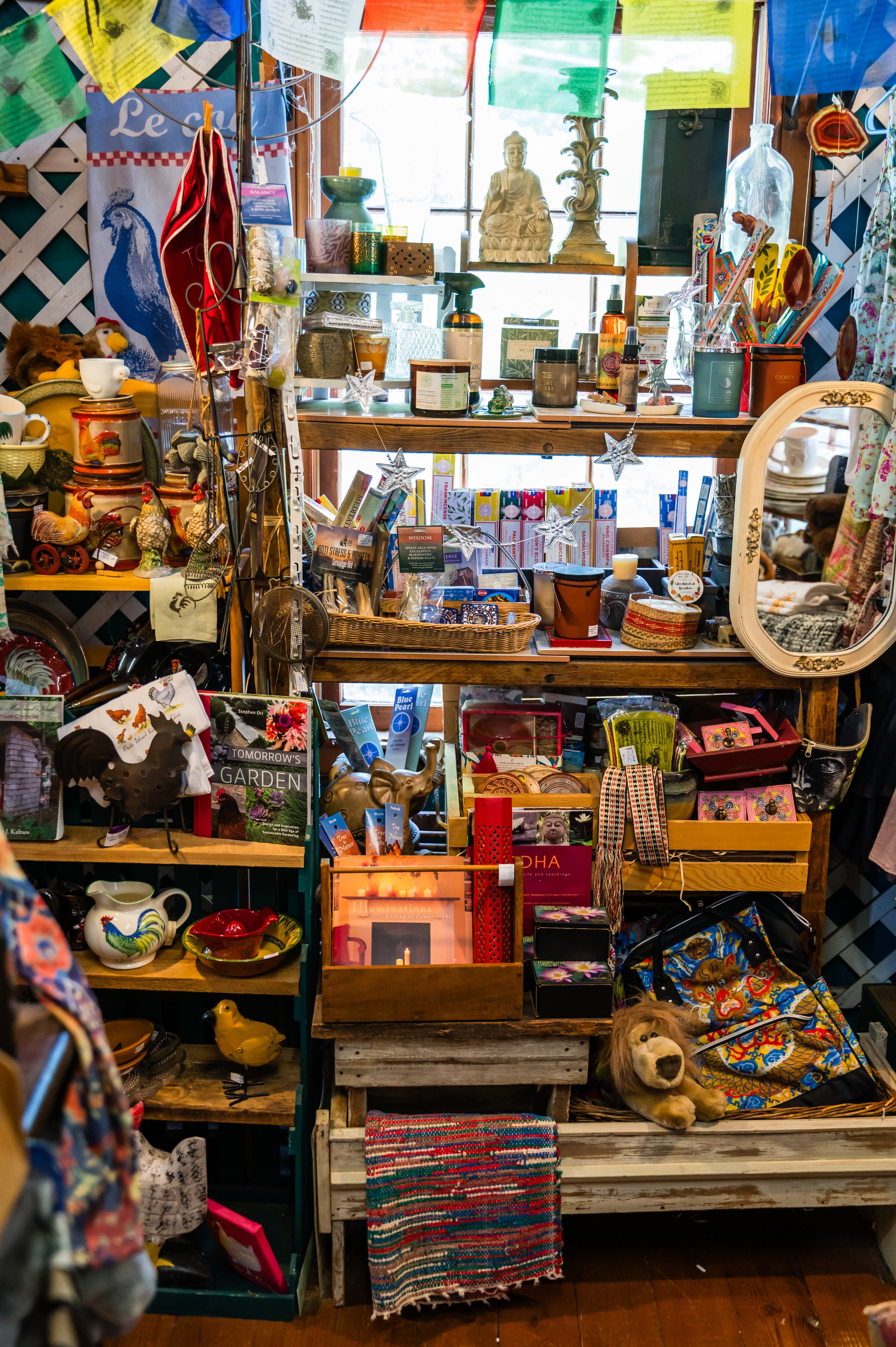 A cluttered display shelf with various decorative items, books, and kitchenware. The shelf has three levels and is decorated with star-shaped ornaments hanging from the middle. There is a dog plush toy lying on the lower level among other miscellaneo