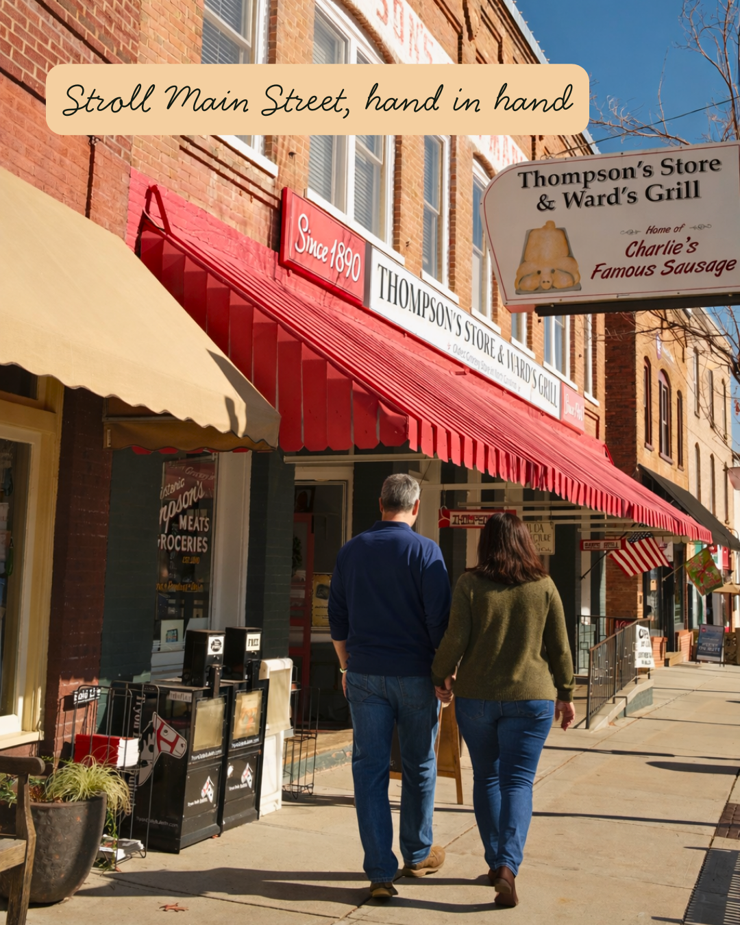 A couple walking hand in hand on a sidewalk in front of a store with a red awning and a sign reading "Thompson's Store & Ward's Grill". The store has a sign indicating it was established in 1890 and is known for Charlie’s Famous Sausage. The scene is sunny with a clear blue sky.