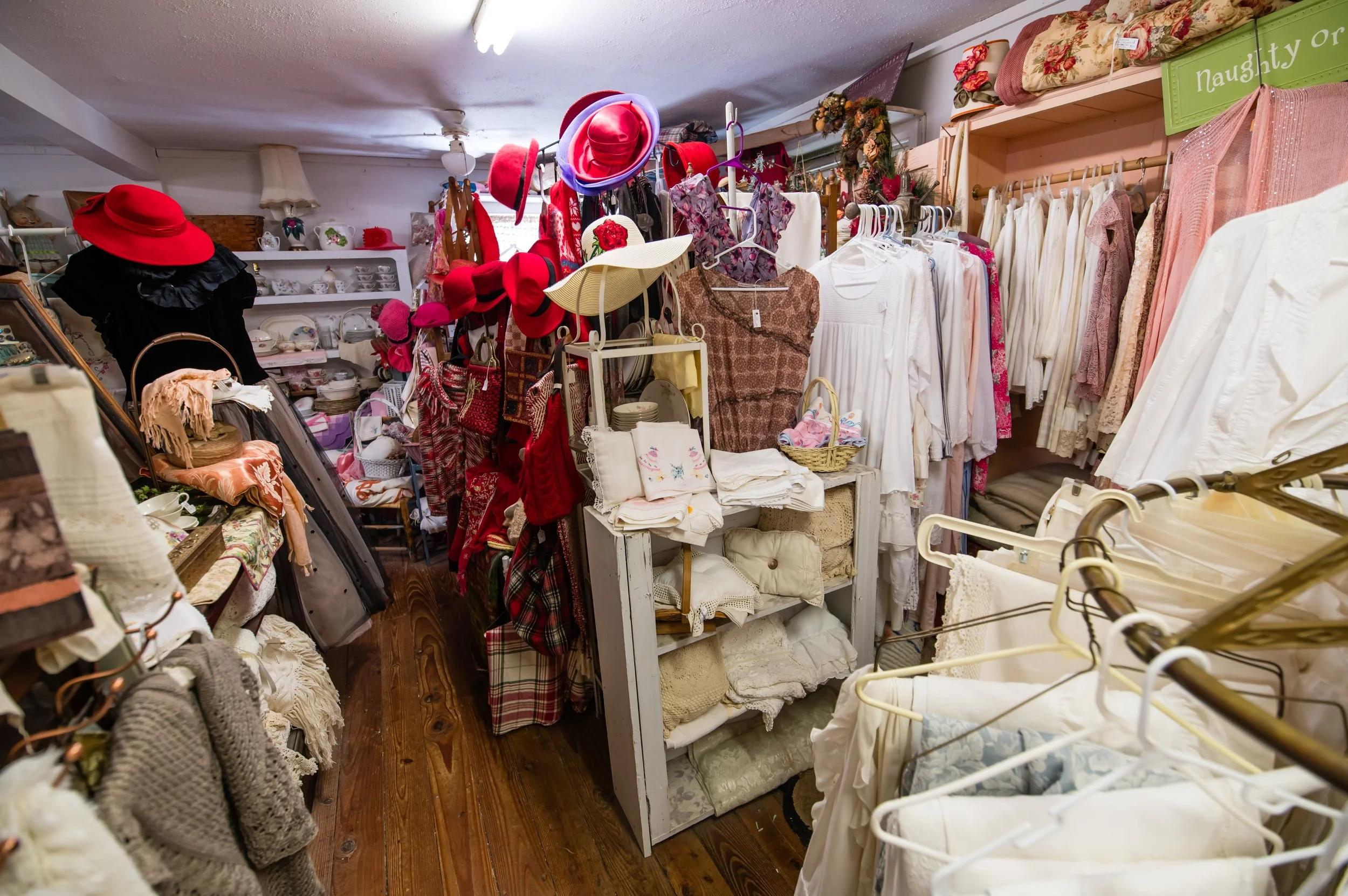 A cluttered thrift store or clothing boutique with various hats, clothing, and accessories on display.
