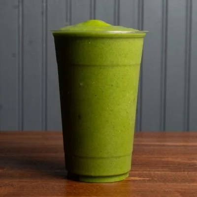 A green smoothie in a clear plastic cup with a domed lid.