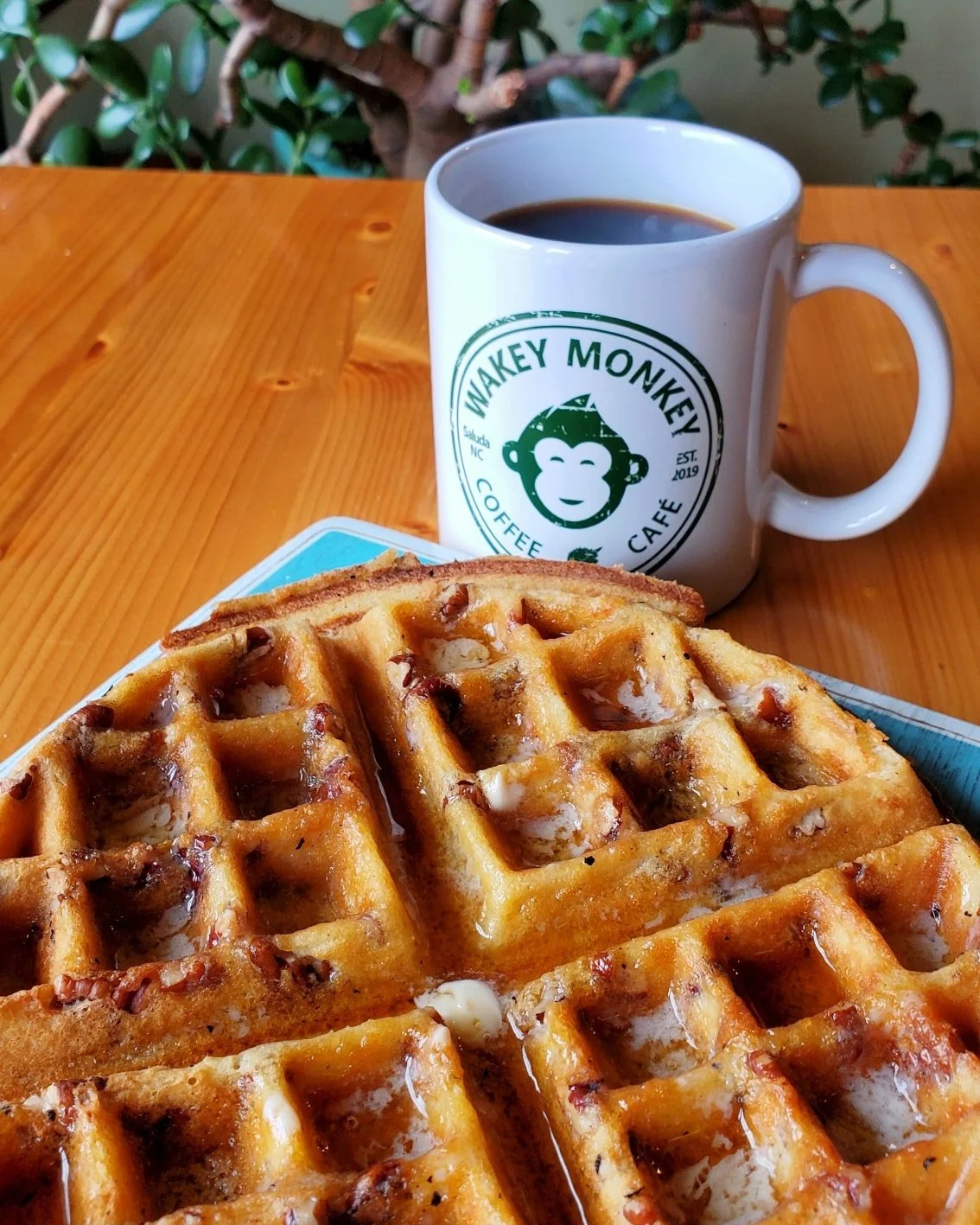 A cup of black coffee and two waffles with syrup and pecans on a plate on a wooden table.