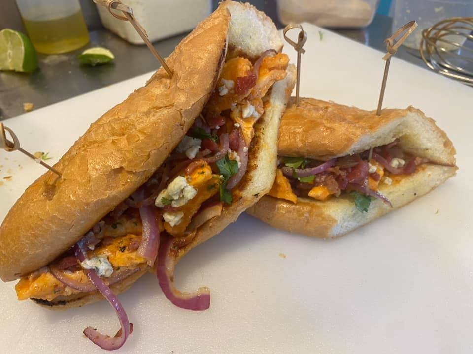 Half of a breakfast sandwich with fried bread, scrambled eggs, cheese, bacon, and red onion, held together with skewers.
