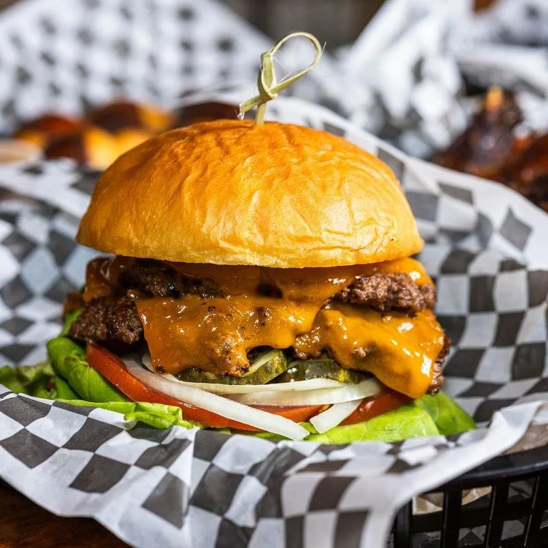 Cheeseburger with lettuce, tomato, onions, pickles, and melted cheese in a bun, served with a toothpick on top.