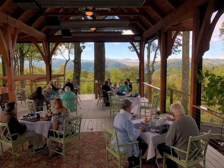 People dining on a covered outdoor deck with a scenic mountain view
