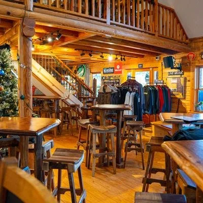Interior of a rustic shop or cafe with wooden furniture, clothing racks, and a staircase leading to a loft area.