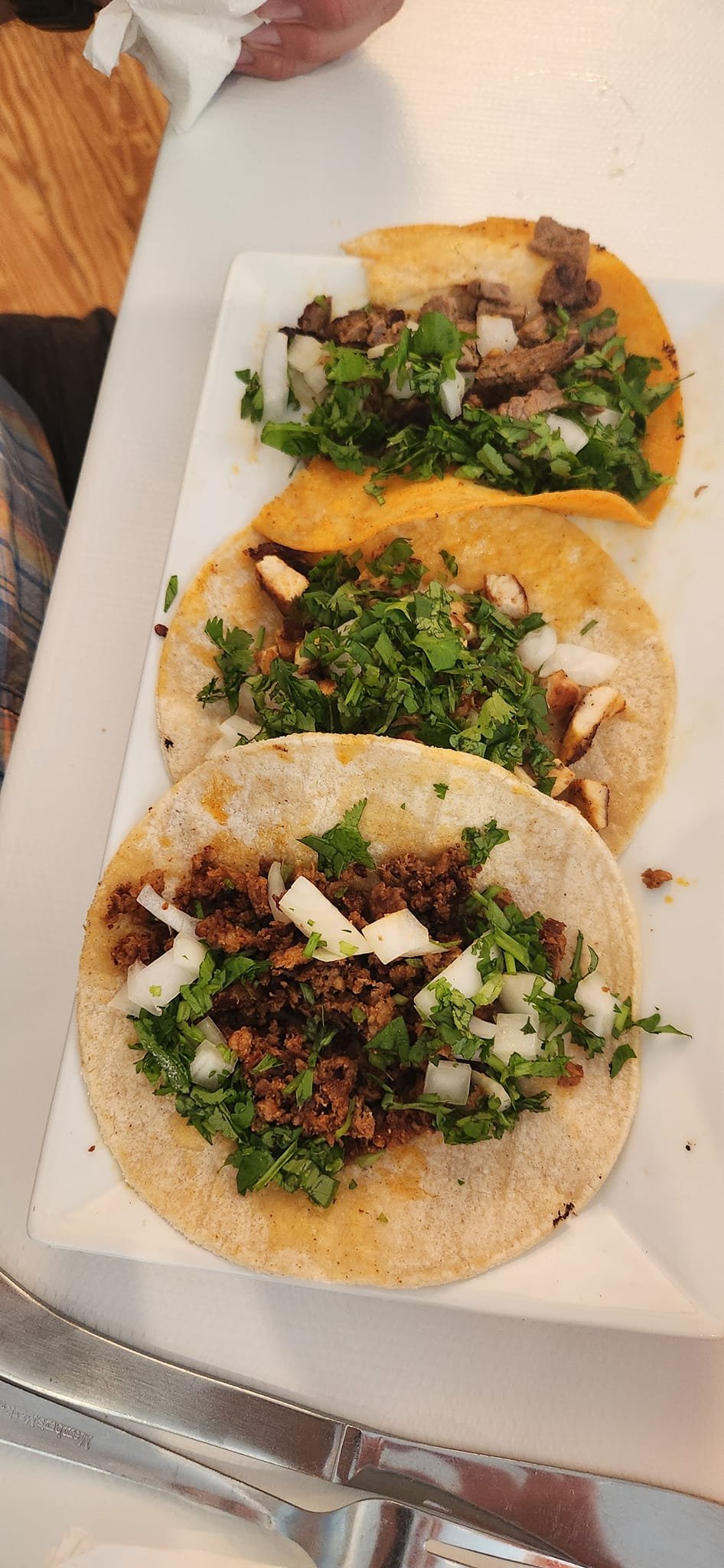 A white rectangular plate with three tacos topped with chopped onions and cilantro, on a white surface.