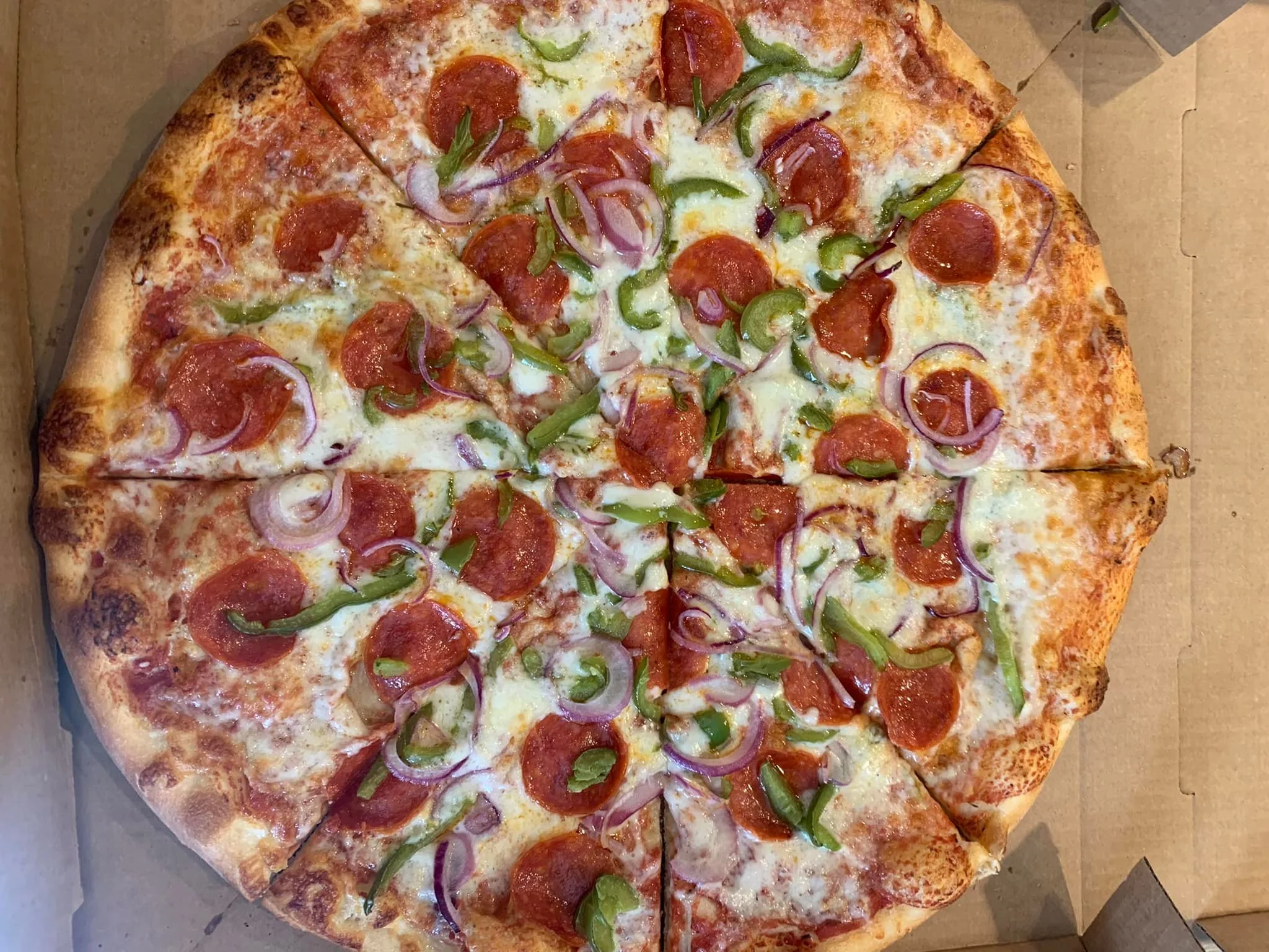A pepperoni pizza with green bell peppers and red onions on top in a cardboard pizza box.