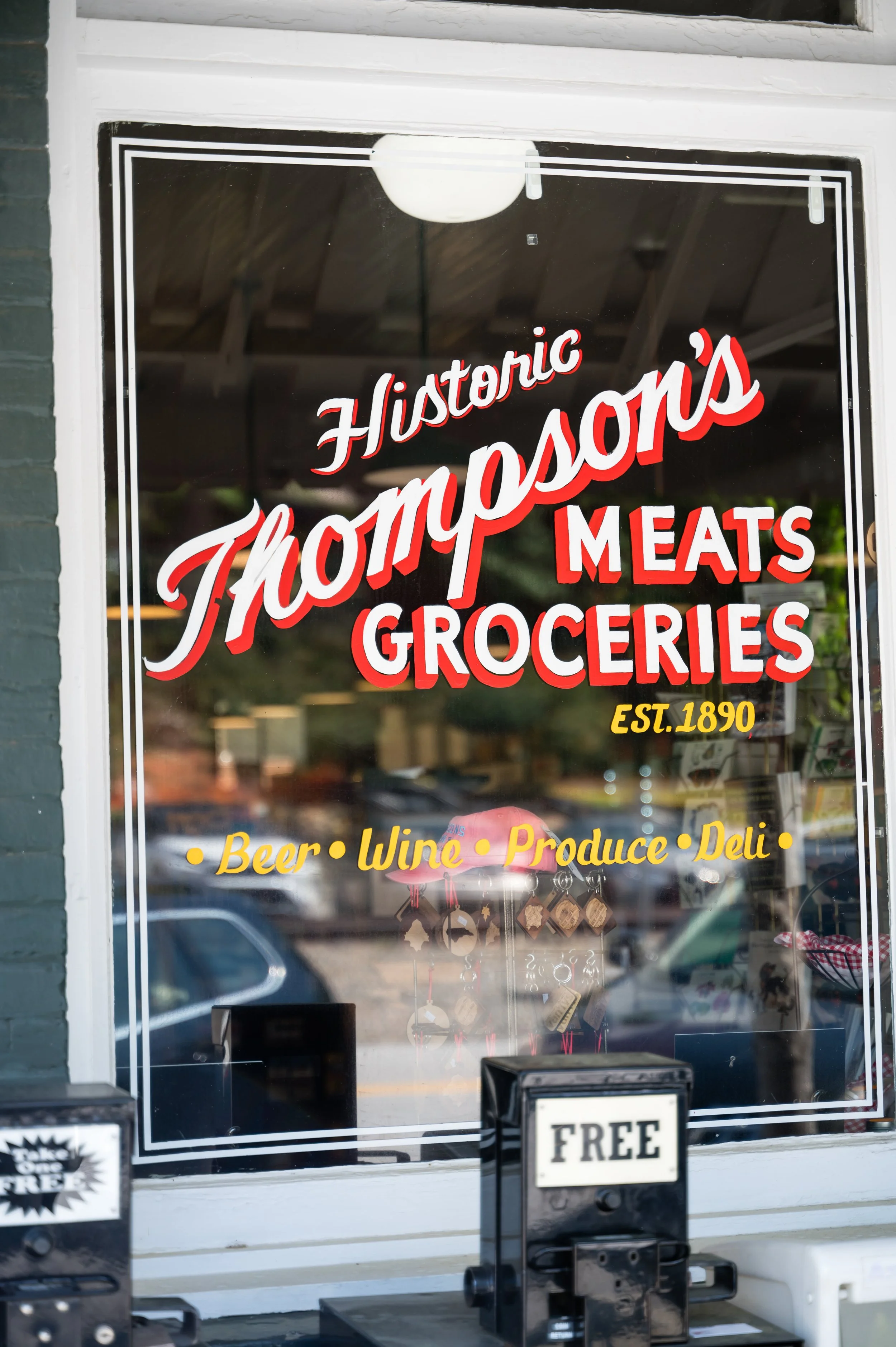 Sign on a store window advertising a historic store that sells meats, groceries, beer, wine, produce, and deli items, established in 1890.