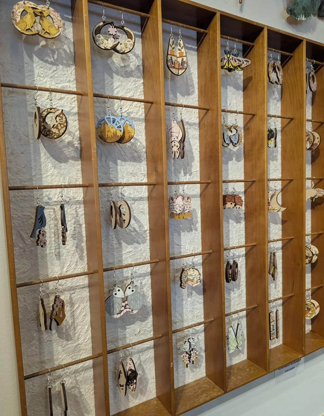 Display of various wooden earrings with nature, animal, and celestial designs hanging on a wooden grid.