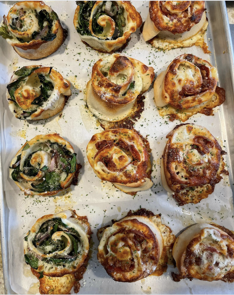 A tray of assorted mini pizza potato skins topped with cheese, pepperoni, vegetables, and herbs.