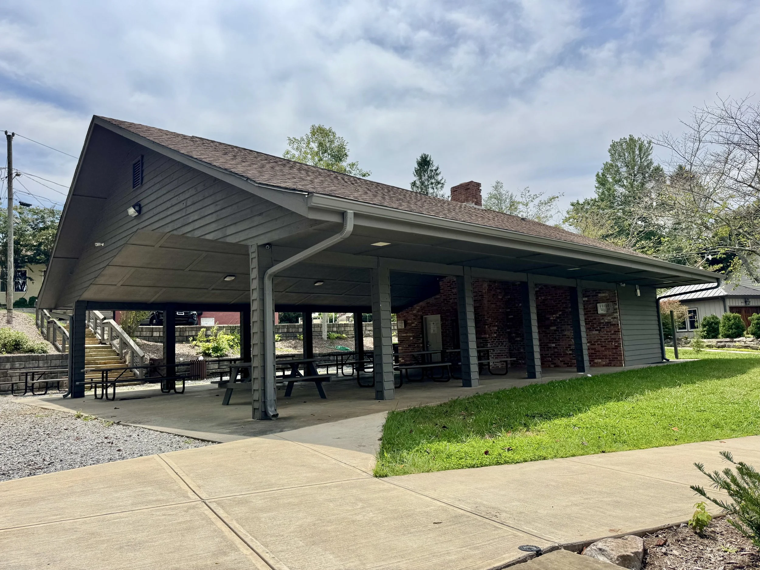 Backyard with covered patio, picnic tables, and surrounding greenery.