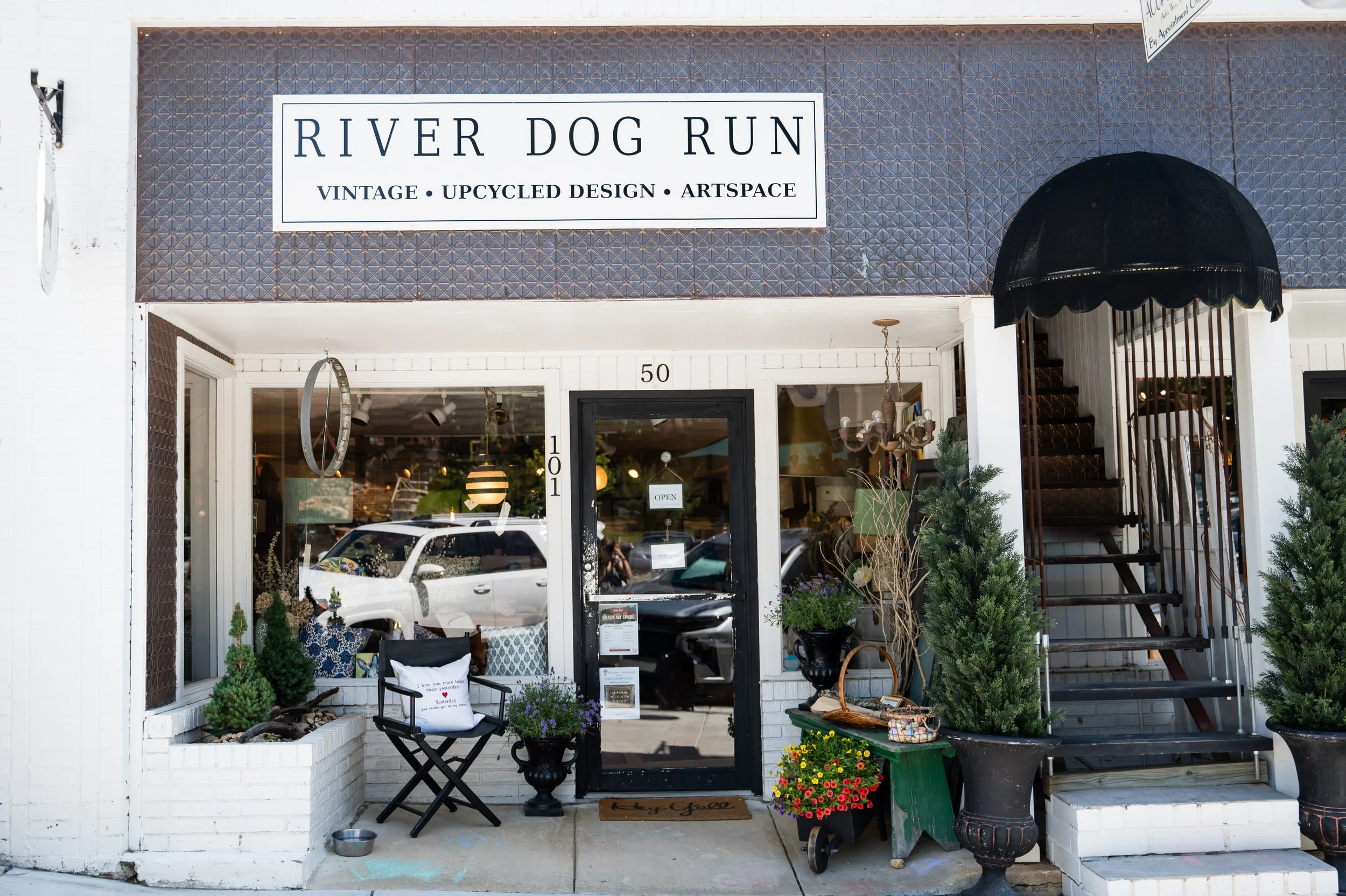 Storefront of River Dog Run featuring vintage, upcycled design, and art space, with decorative plants and seating outside