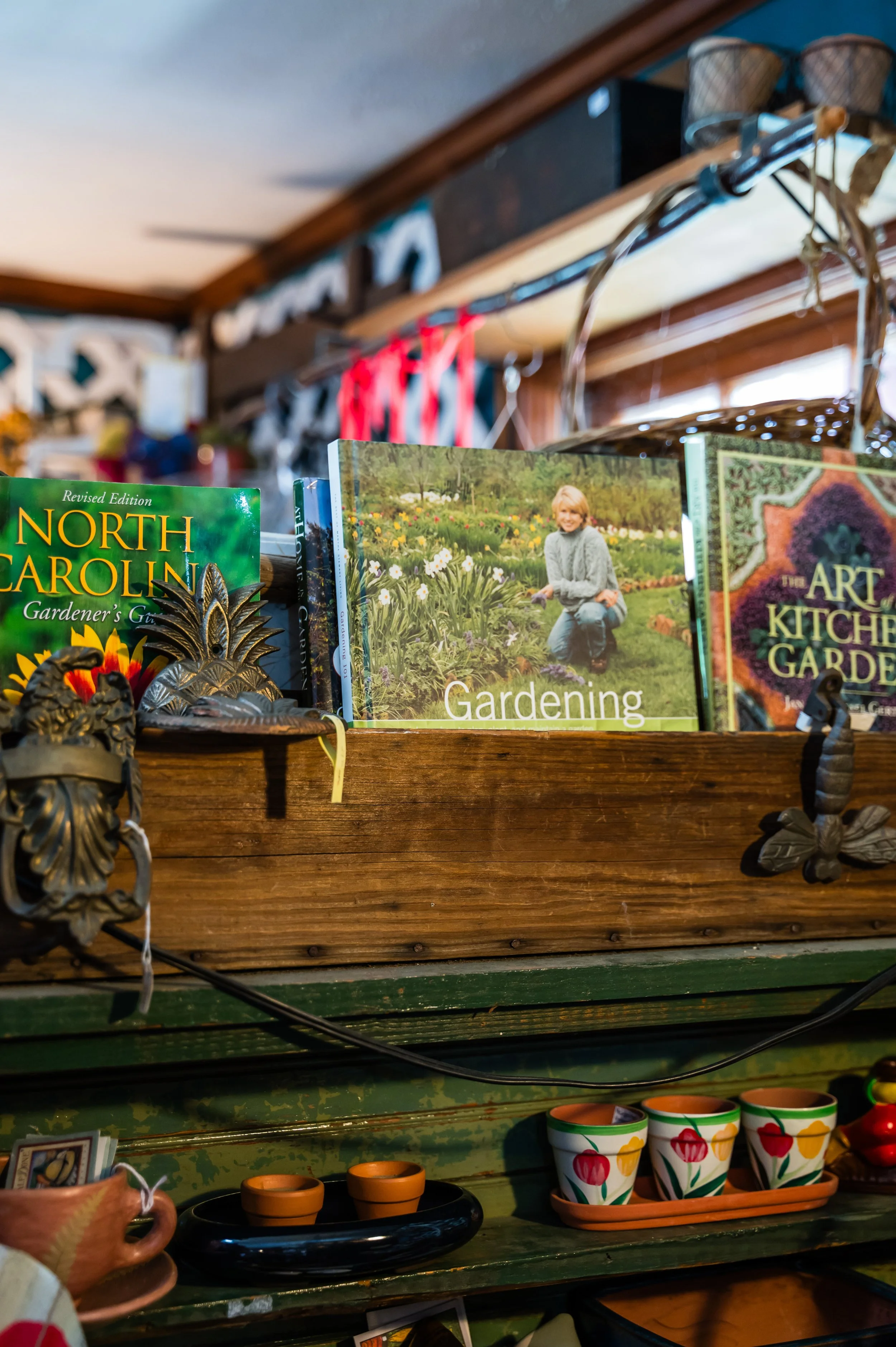 Books about gardening, a decorative pineapple, and pottery displayed on wooden shelves with a rustic, cozy store interior.