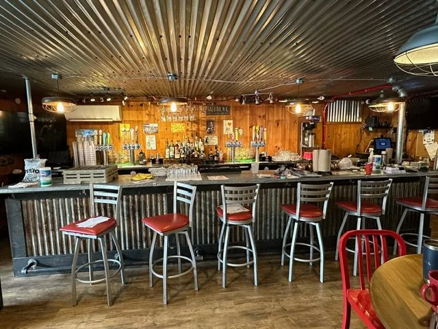 Empty bar with metal bar stools and red-cushioned seats in a rustic wooden interior.