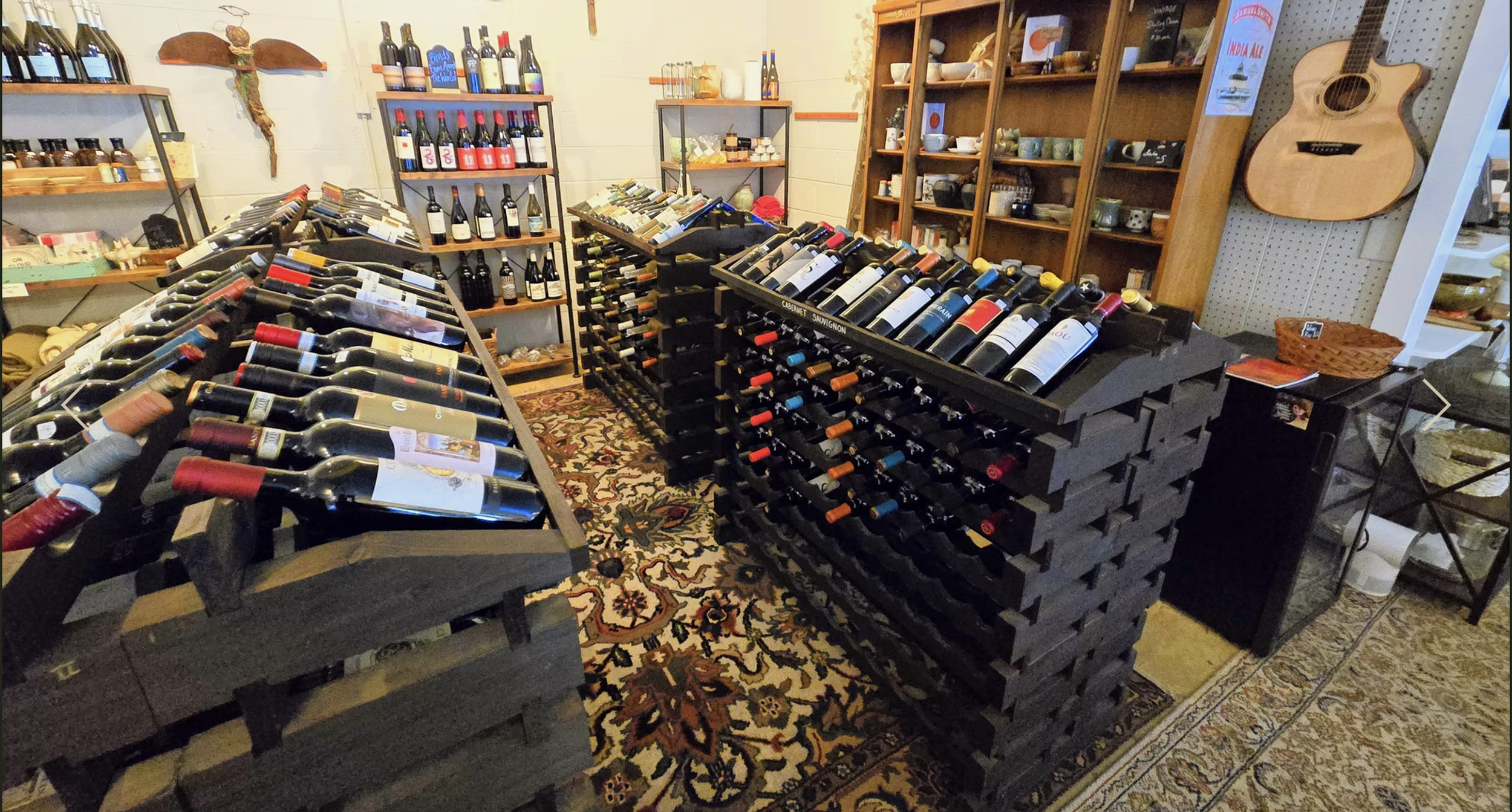 A store display with multiple shelves and racks filled with bottles of wine, along with some other items such as ceramics, a guitar, and small decorative objects.