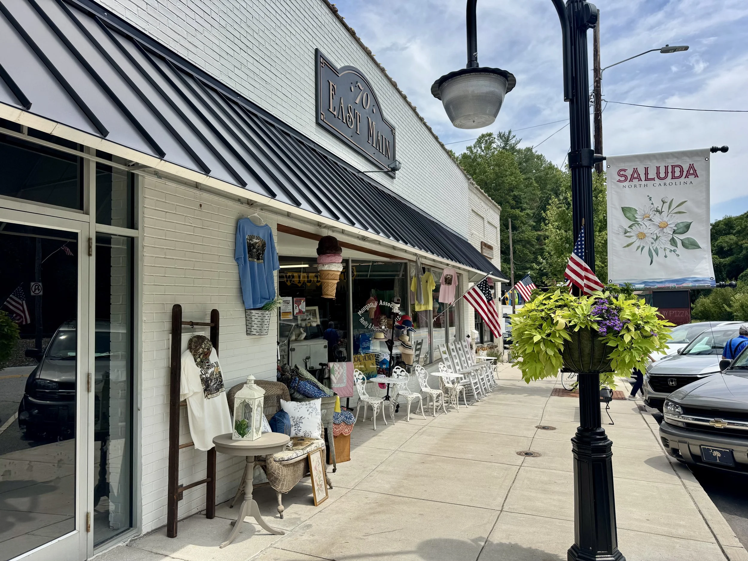 Street view of a small shop with outdoor display, American flags, and a sign that reads 'Frosty & Main.'