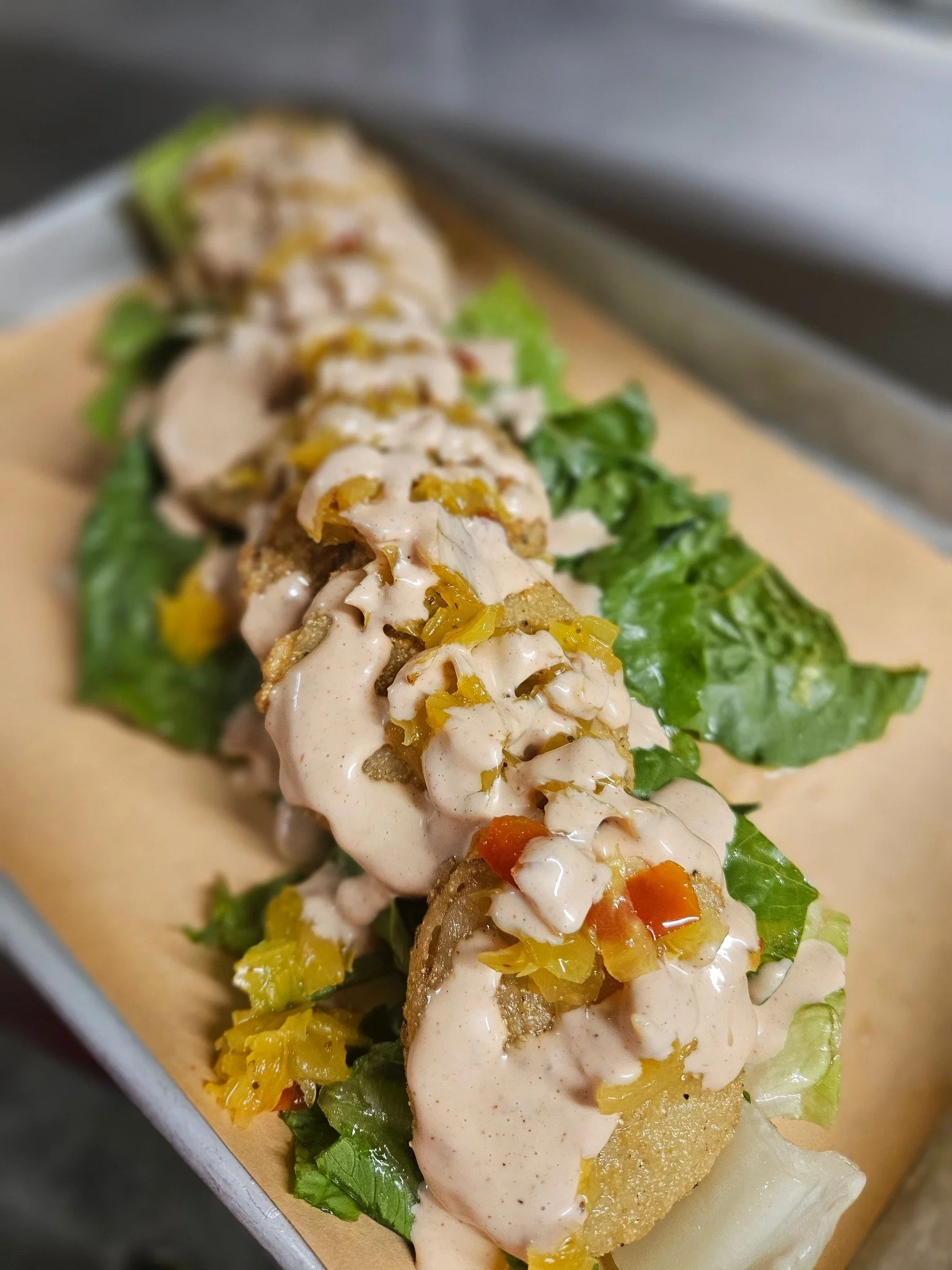 Close-up of a gourmet sandwich with lettuce, grilled chicken, yellow chutney, and creamy sauce on toasted bread.