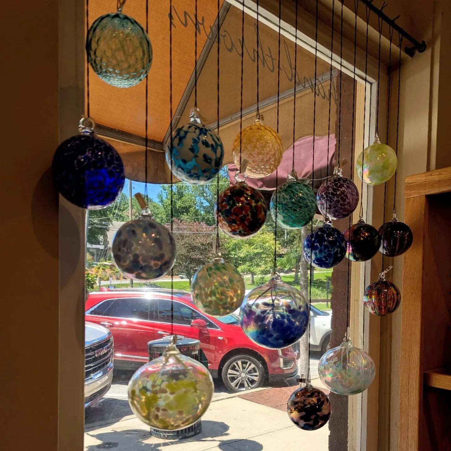 Colorful glass orbs hanging in a window, with a view of cars and trees outside.