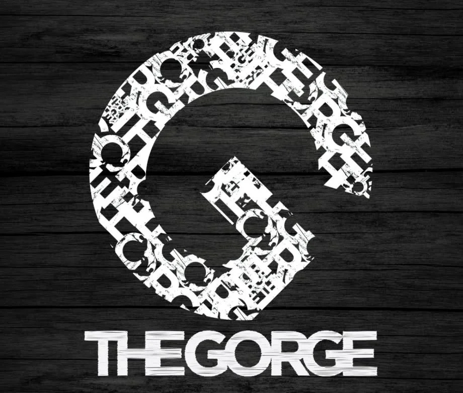 A logo with a recycling symbol composed of letters and words, with the text 'THE GEORGE' below it, on a dark wooden background.