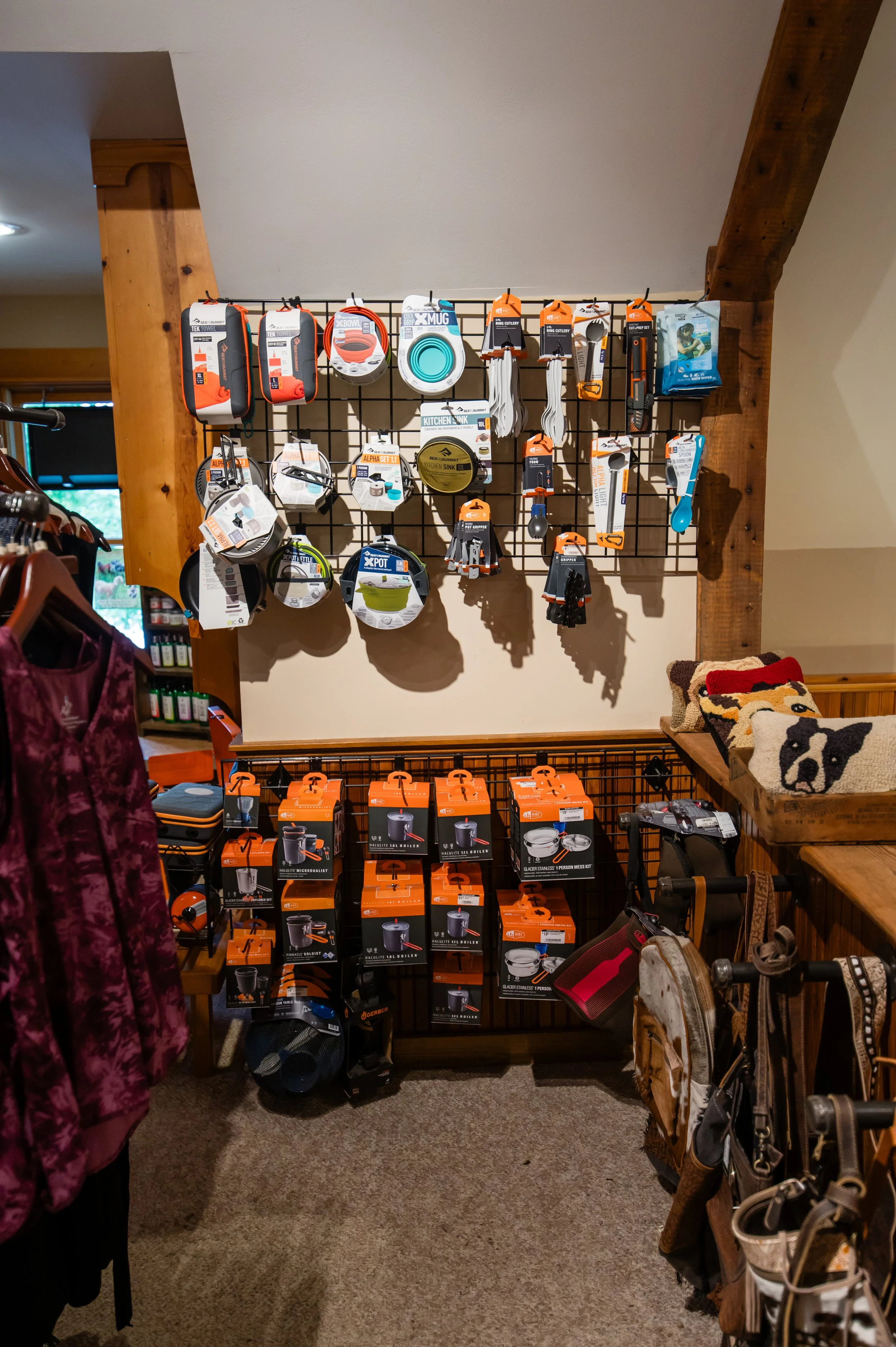 Store display with various outdoor and camping accessories hanging on a black grid wall, including portable stoves, cookware, and utensils.