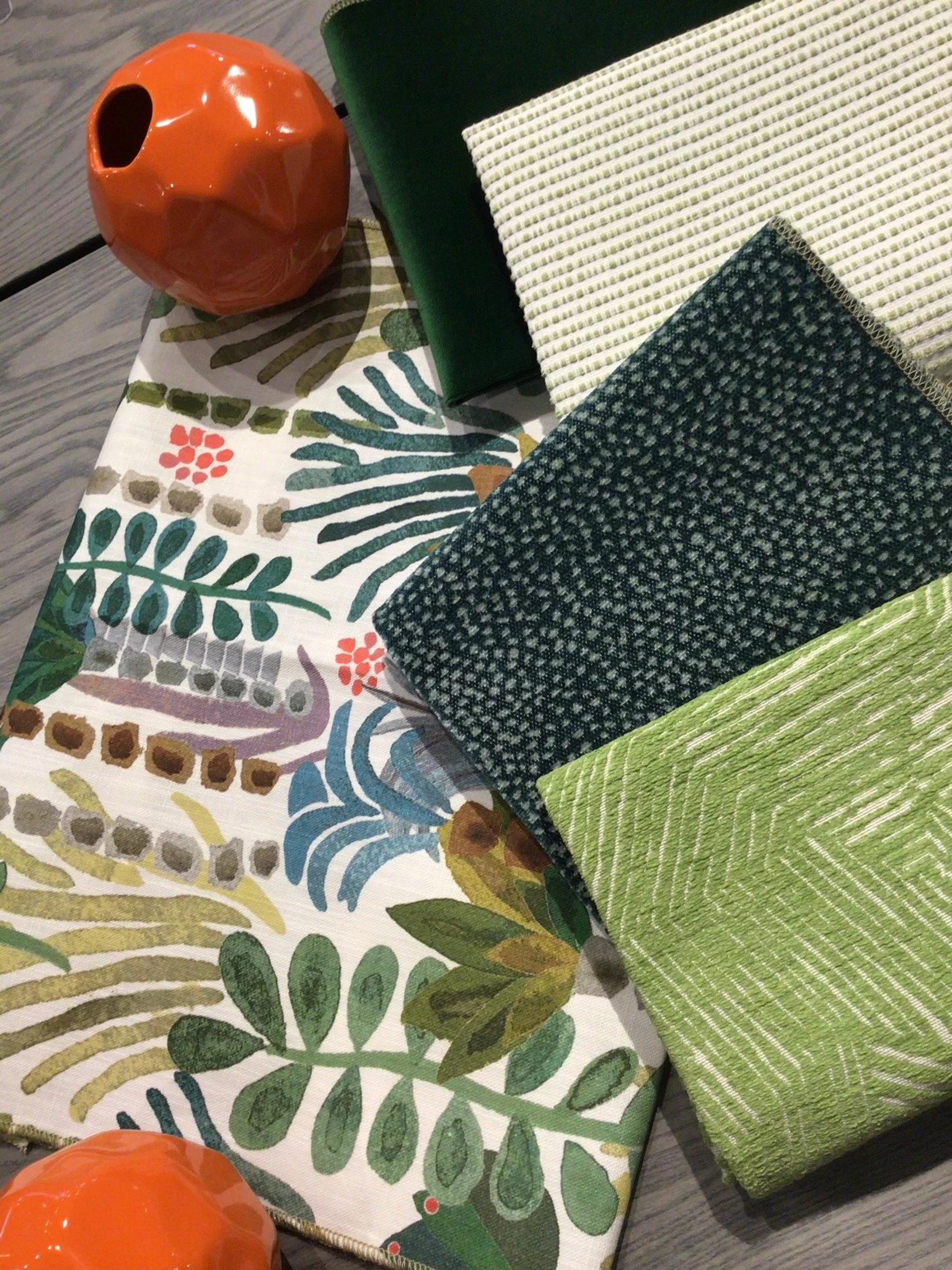 A flat lay of various fabric swatches with different patterns and textures, a decorative orange vase, and a green surface.