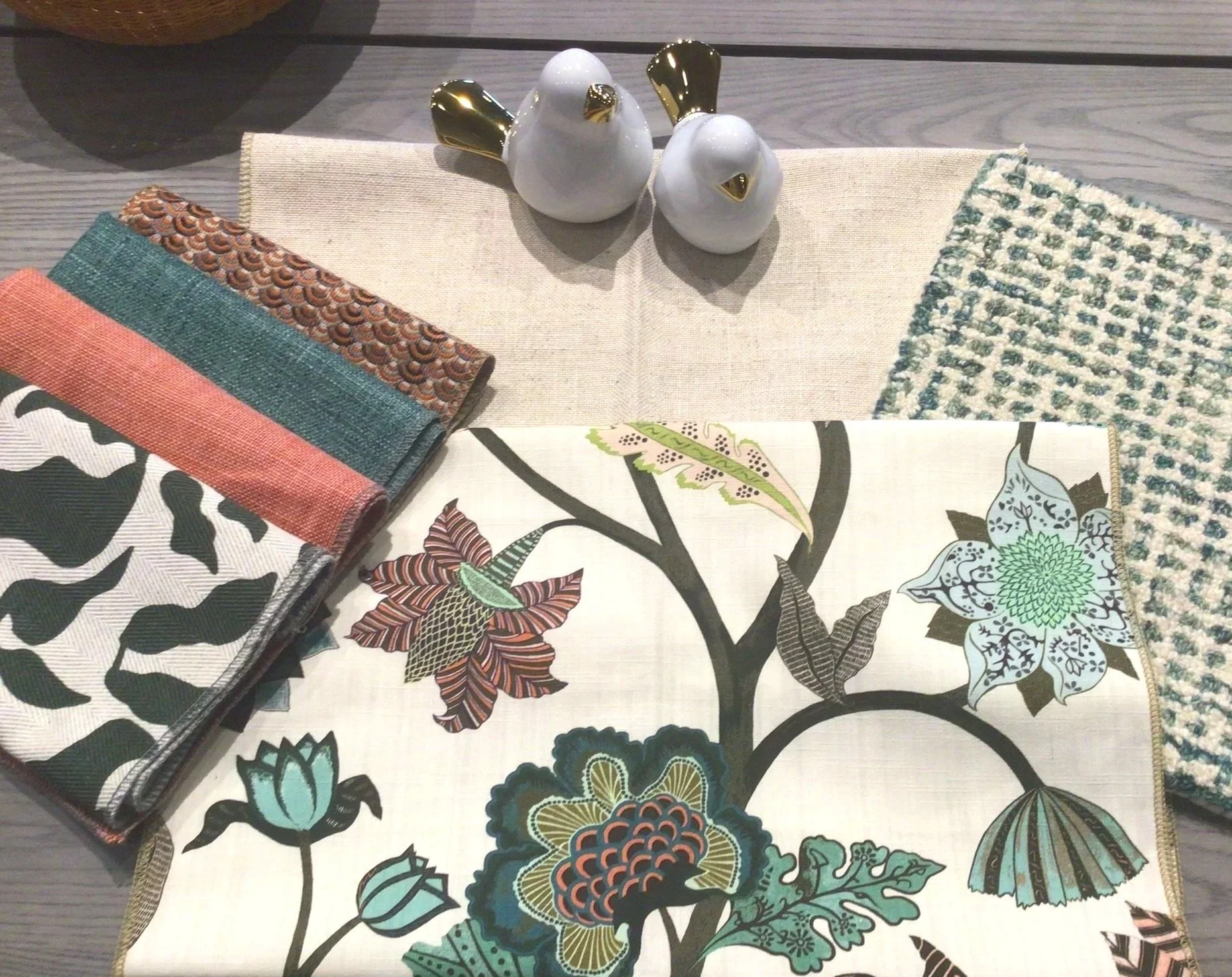 Decorative fabric samples, ceramic bird figurines, and textured tablecloths on a wooden surface.