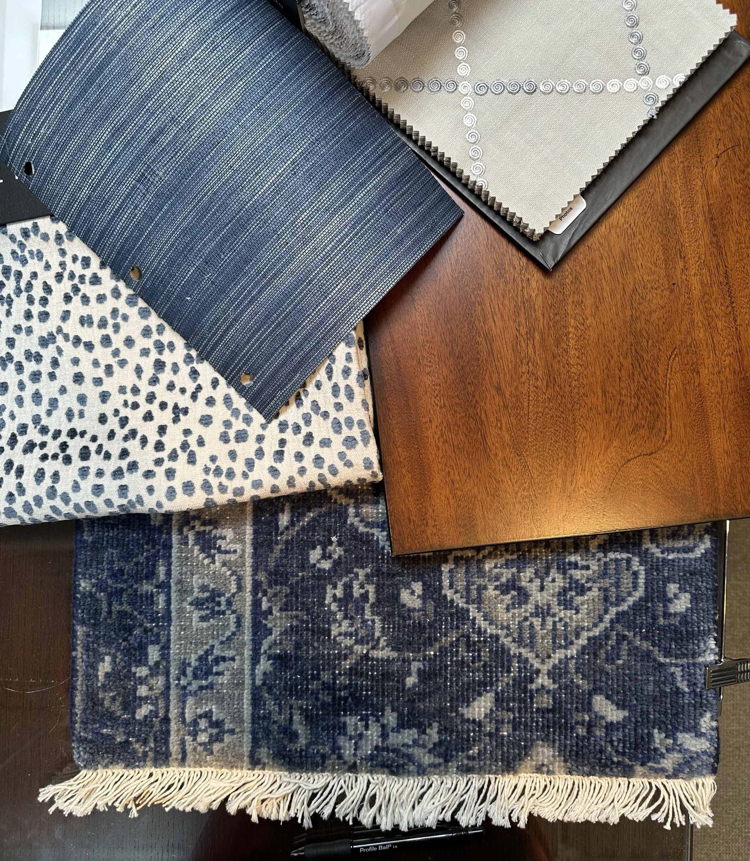 A collection of fabric samples, a wooden table piece, and a small patterned rug displayed on a dark wooden surface.