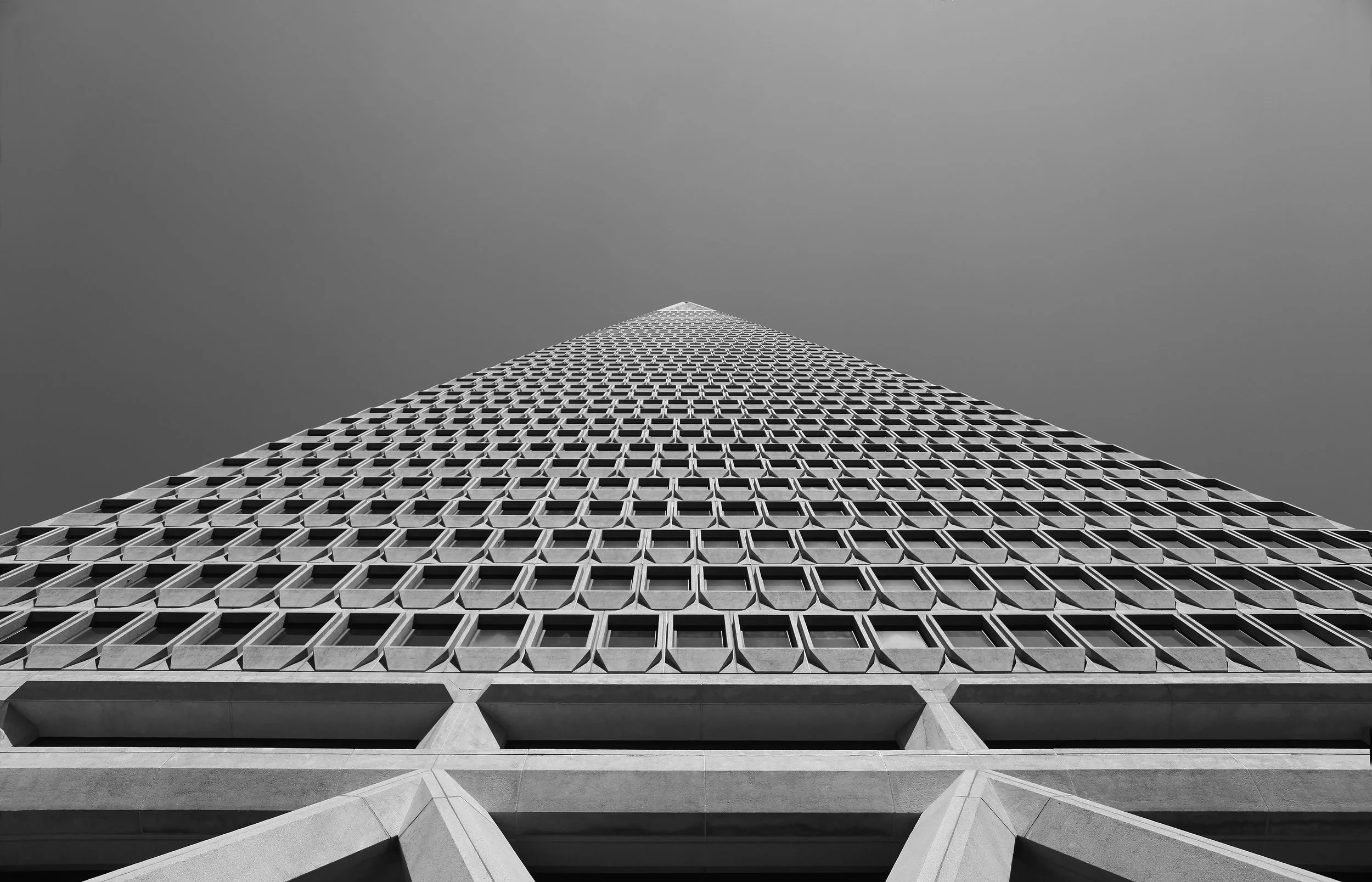 Looking up at a tall modern skyscraper with a grid-like pattern of windows, extending upward under a clear sky.