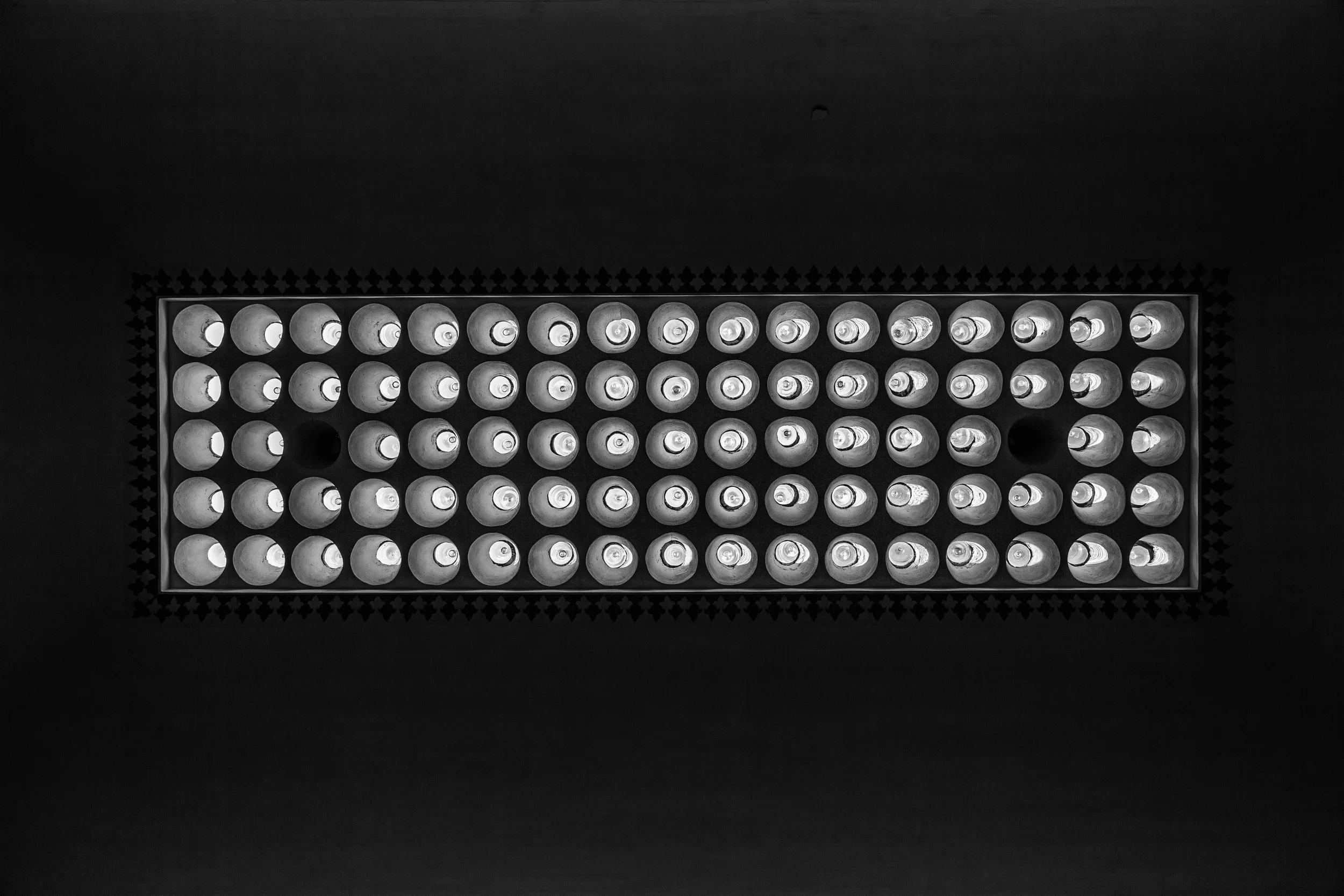 Overhead view of a rectangular grid of light bulbs with some bulbs turned on and off, casting shadows on a dark background.