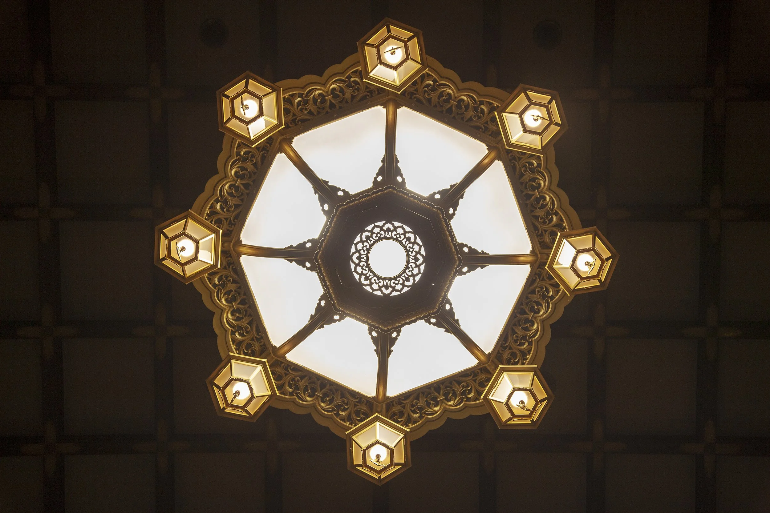 Ornate chandelier with multiple lights hanging from ceiling with decorative trim.