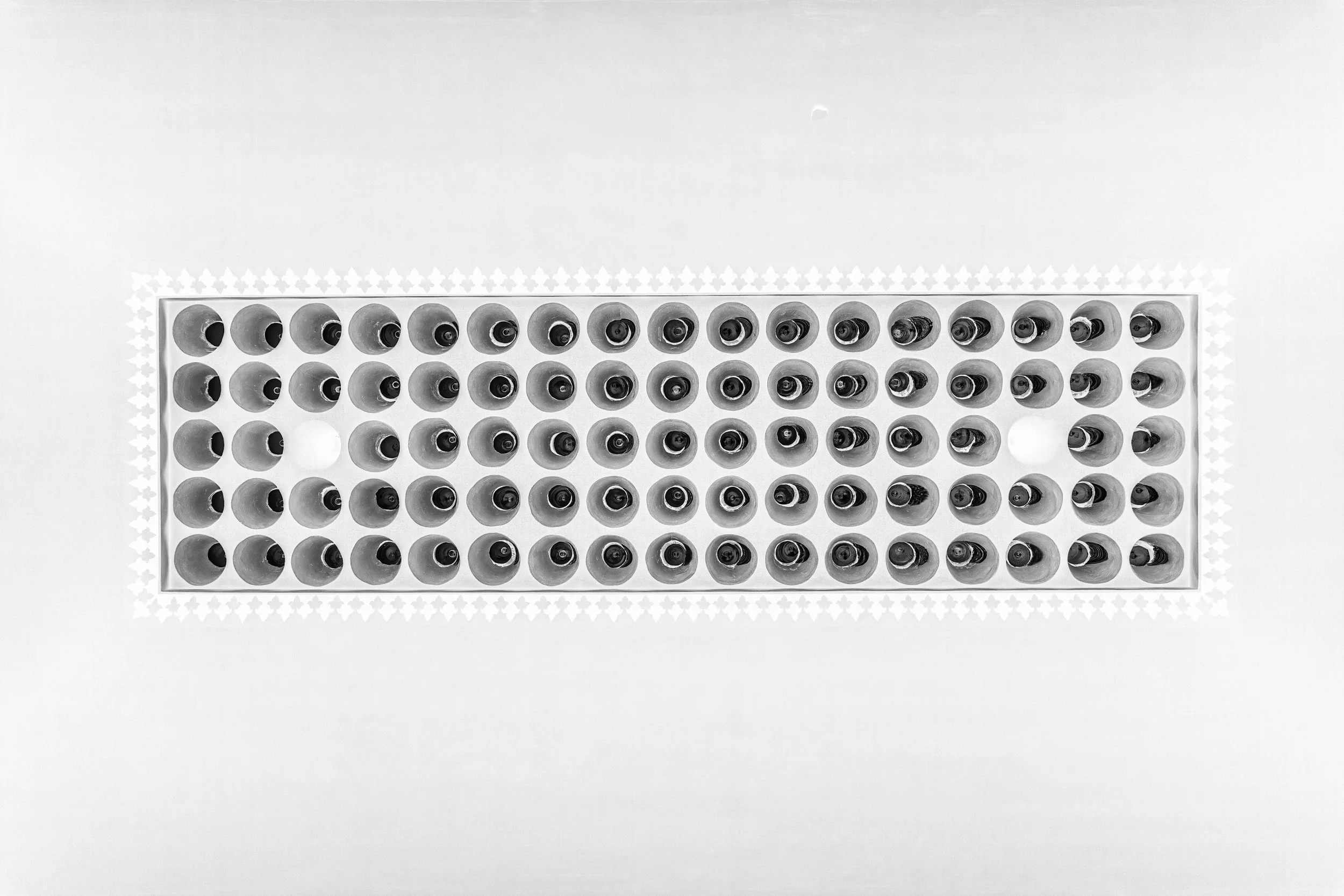 A top-down view of a rectangular box with multiple small bottles arranged in a grid pattern, with two white objects visible among the bottles.