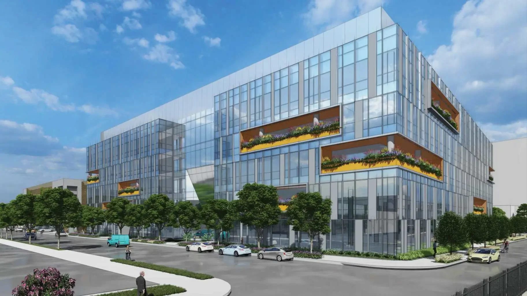Modern multi-story glass office building with colorful flower planters in rectangular openings, surrounded by trees, parked cars, and people walking outside on a sunny day.