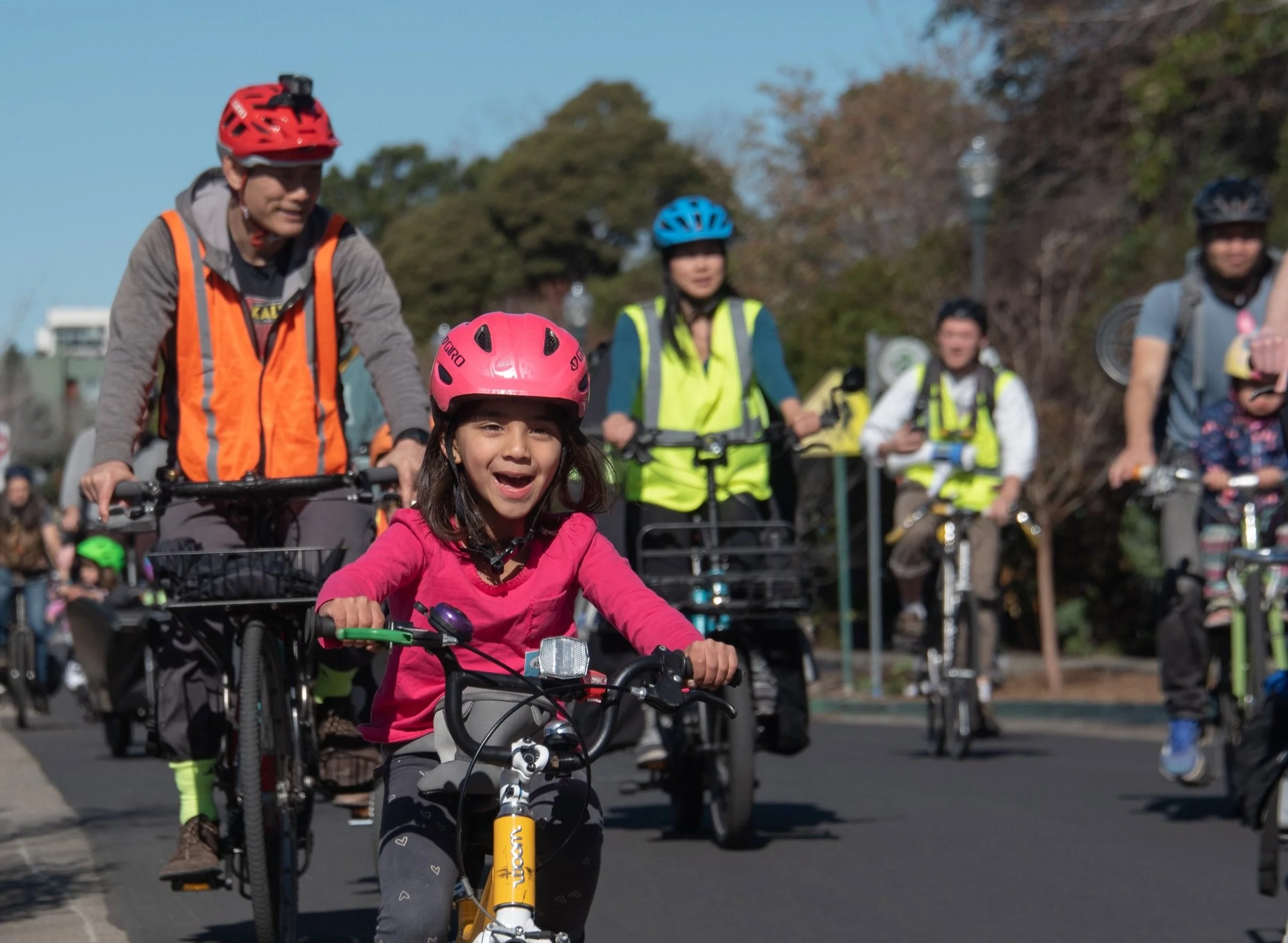 Group of people riding bikes outdoors on a sunny day, wearing helmets and safety vests.
