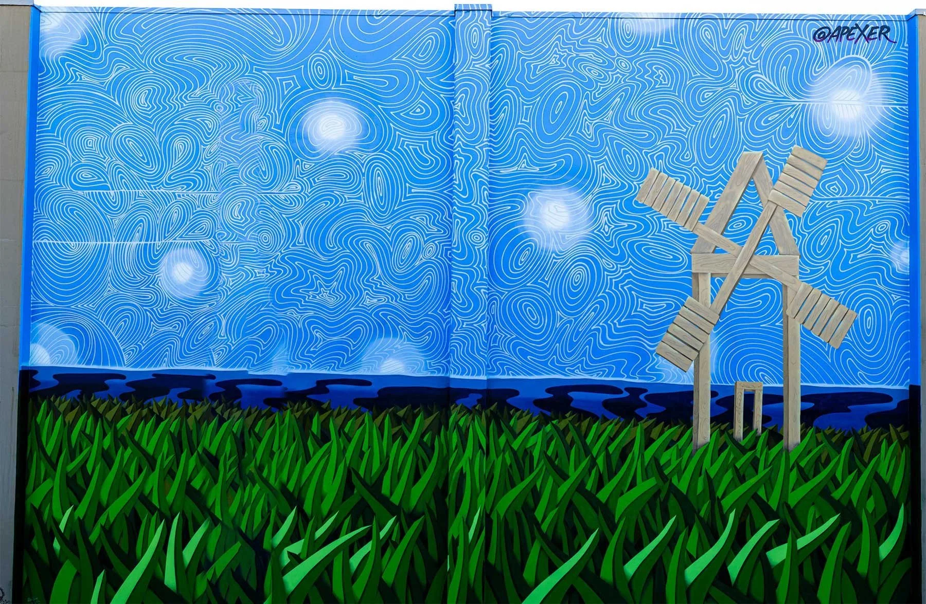 Colorful art mural featuring green grass at the bottom, a blue background with white contour lines, a dark blue river or waterway, and a wooden windmill on the right side, with the word '@APEXER' written in the top right corner.