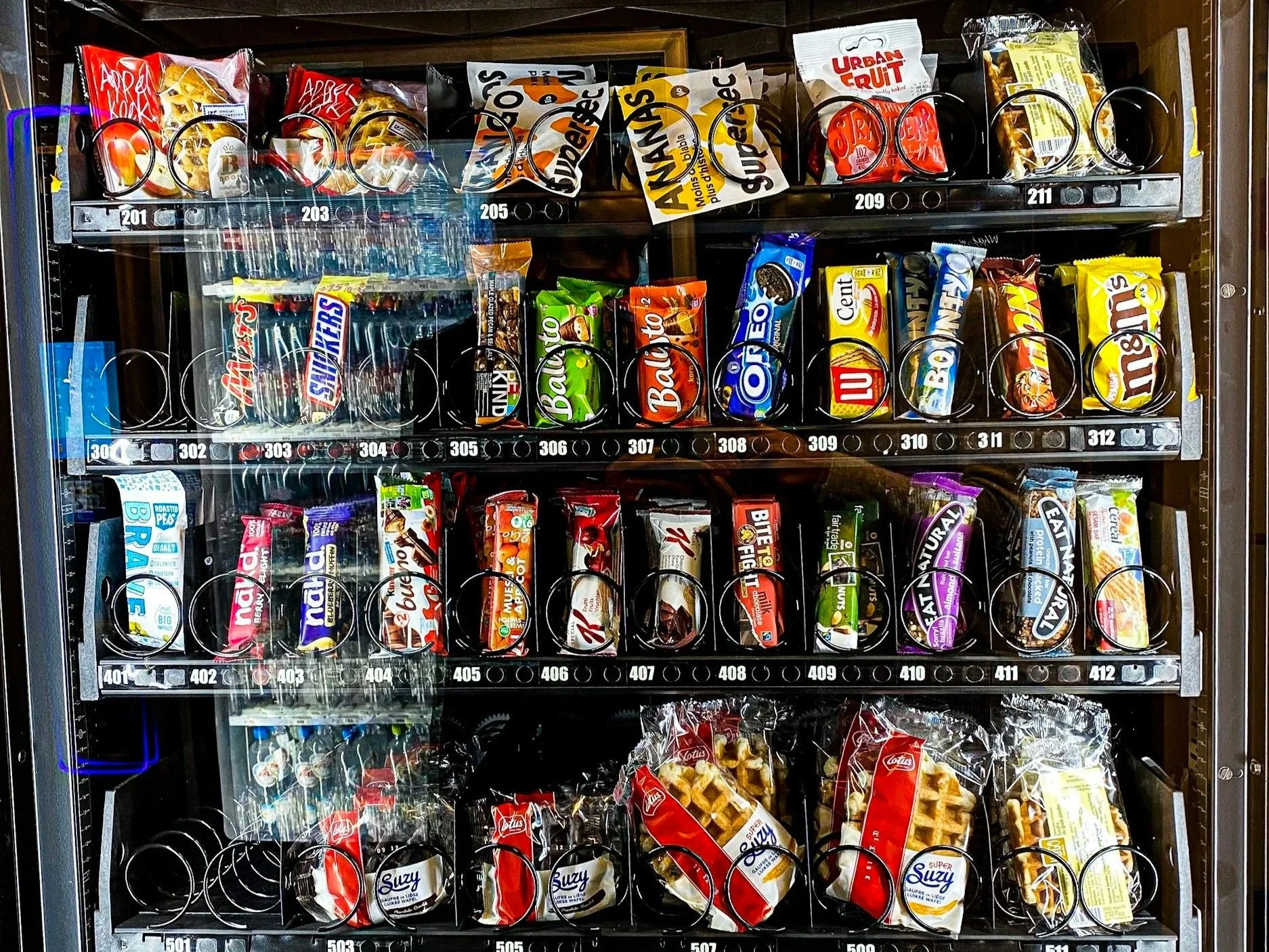 A vending machine filled with various snacks including cookies, chips, and candies in a glass-fronted vending machine.