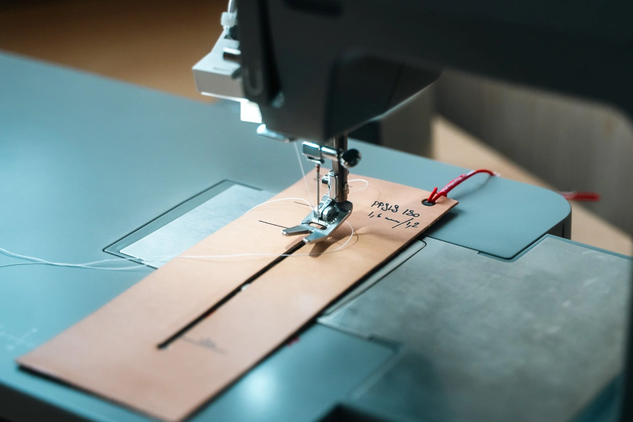 Une machine à coudre cousant un morceau de tissu marron clair avec une note manuscrite attachée dessus.