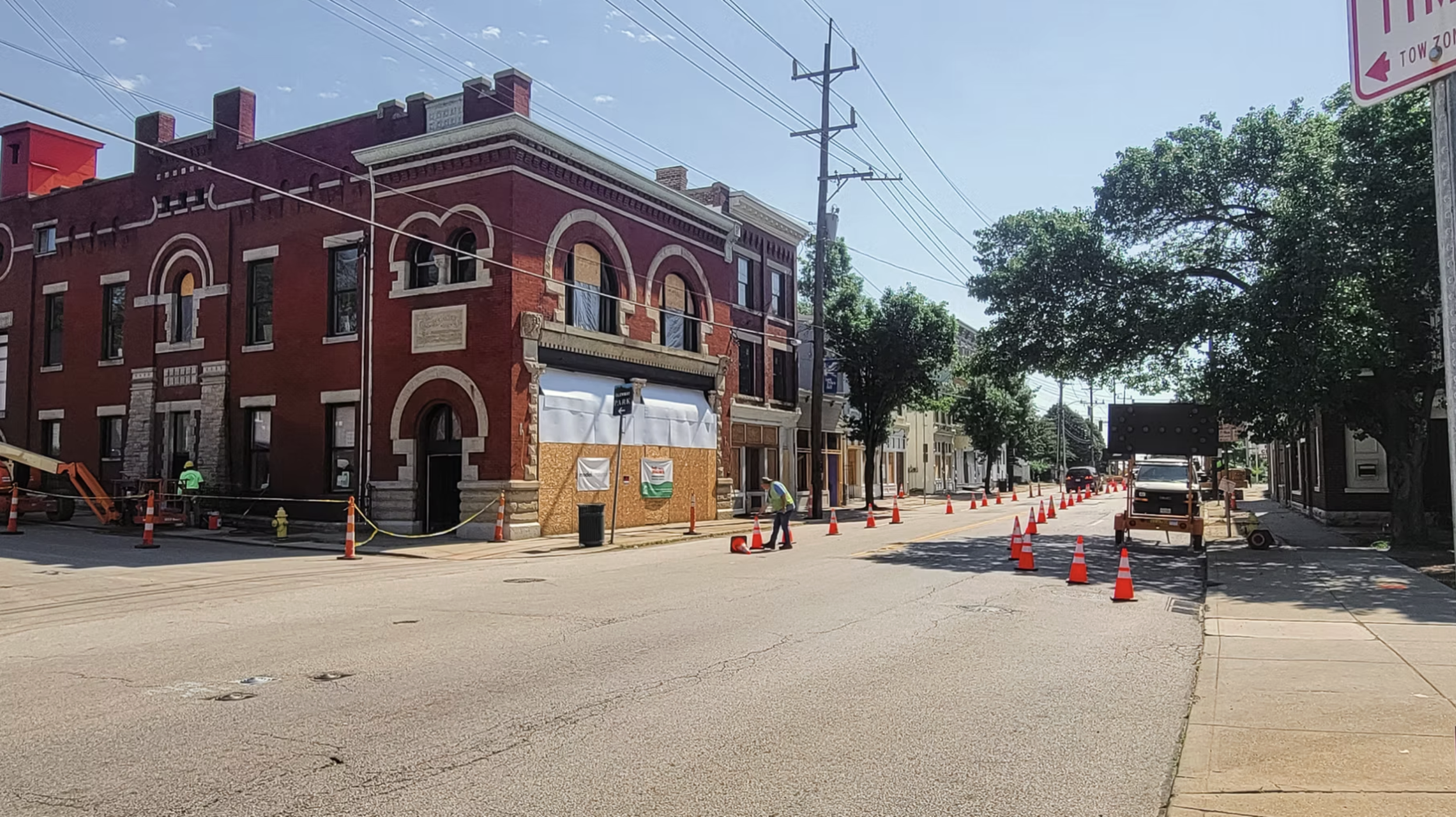Construction workers and orange traffic cones on a city street with partially renovated buildings and trees.