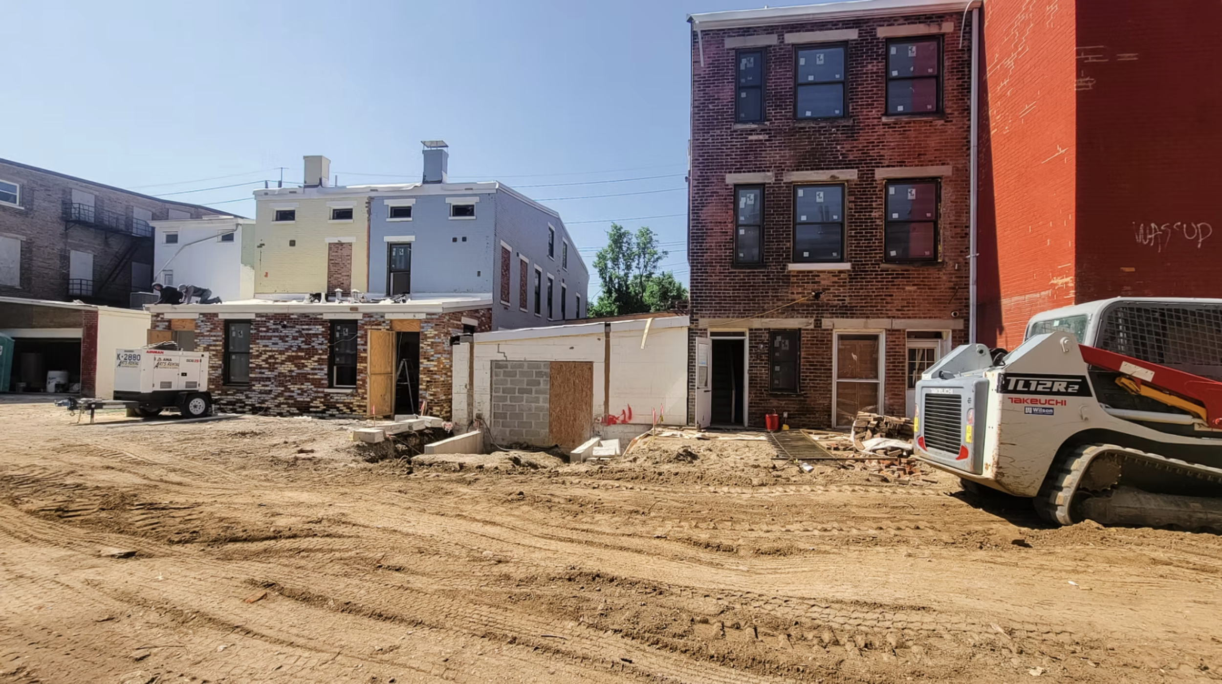 Construction site with old brick buildings being renovated or rebuilt, construction equipment, and dirt ground.