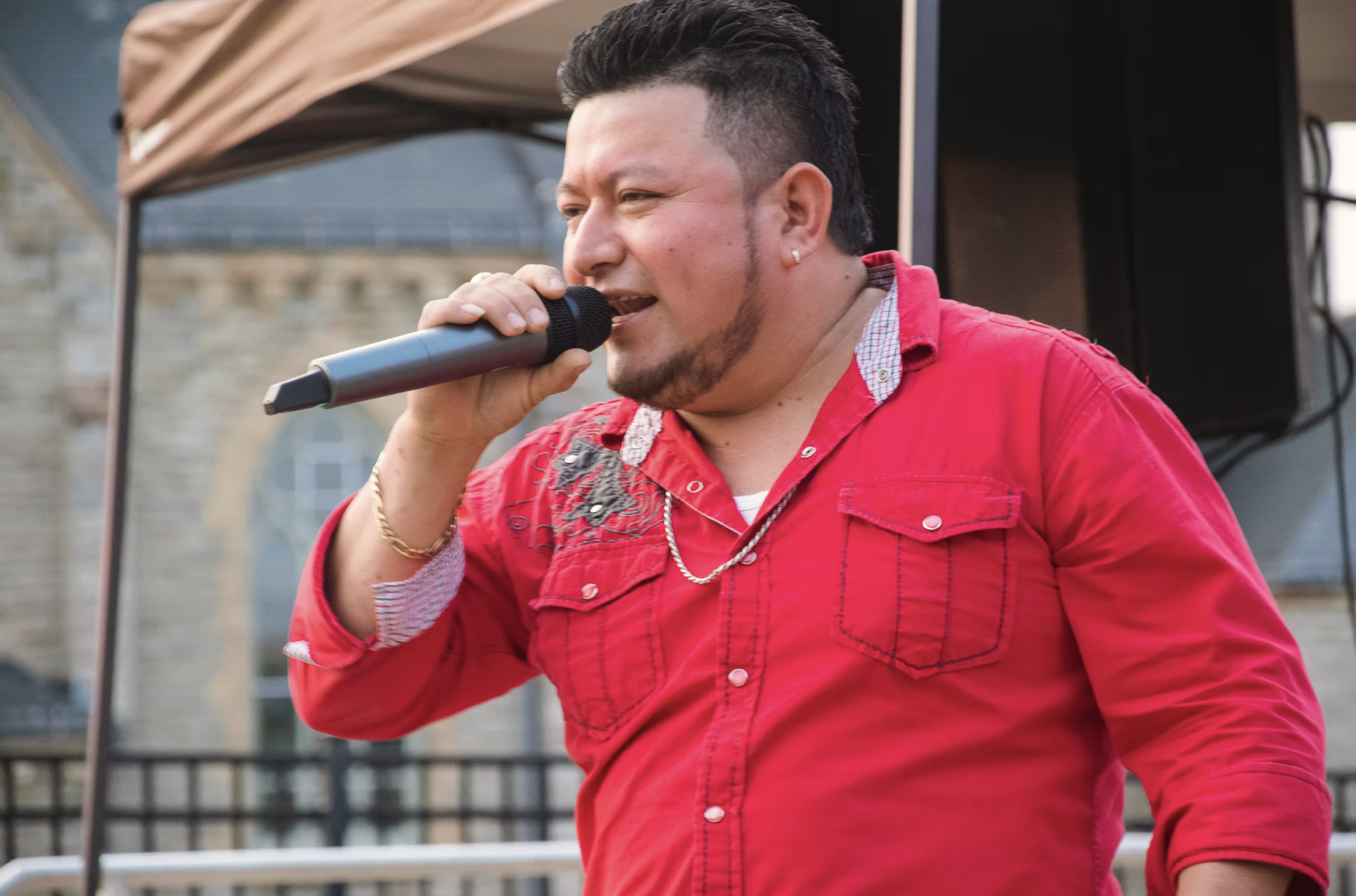 A man in a red shirt singing into a microphone outdoors.