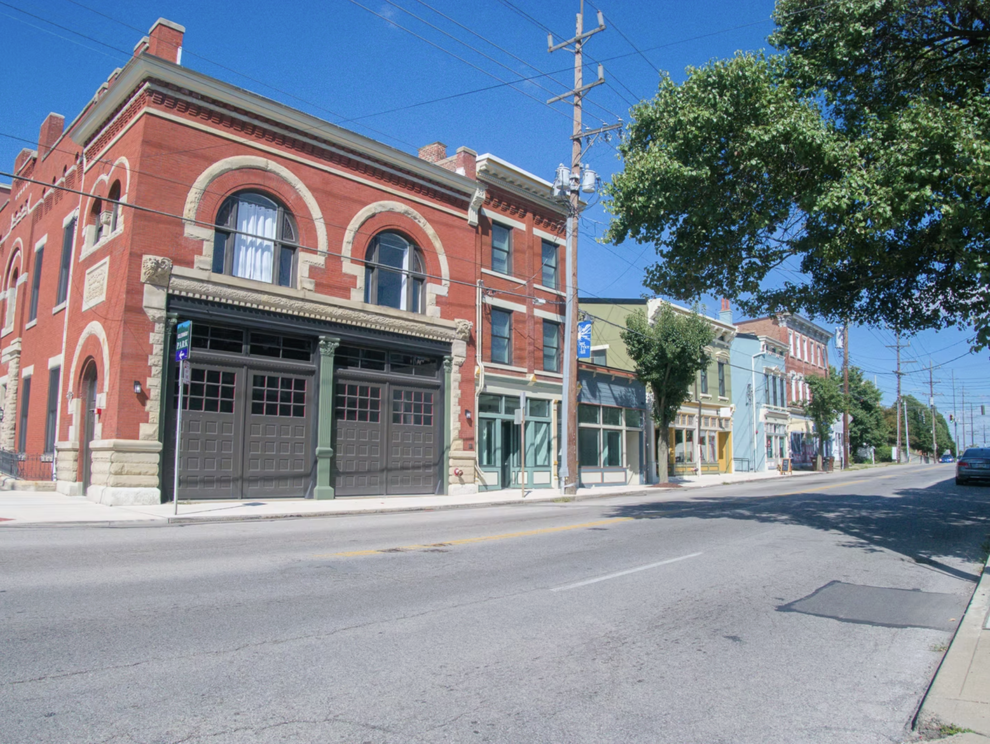 A street view with colorful historic buildings, trees, and parked cars under a clear blue sky.