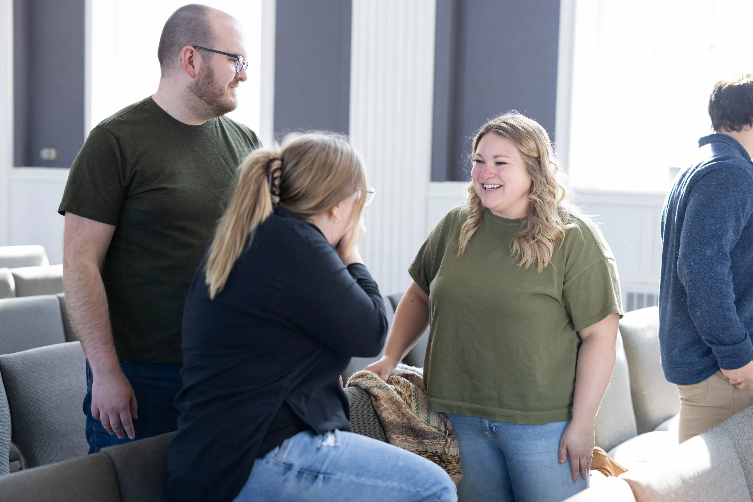 Group of people talking and laughing in a bright room with large windows.