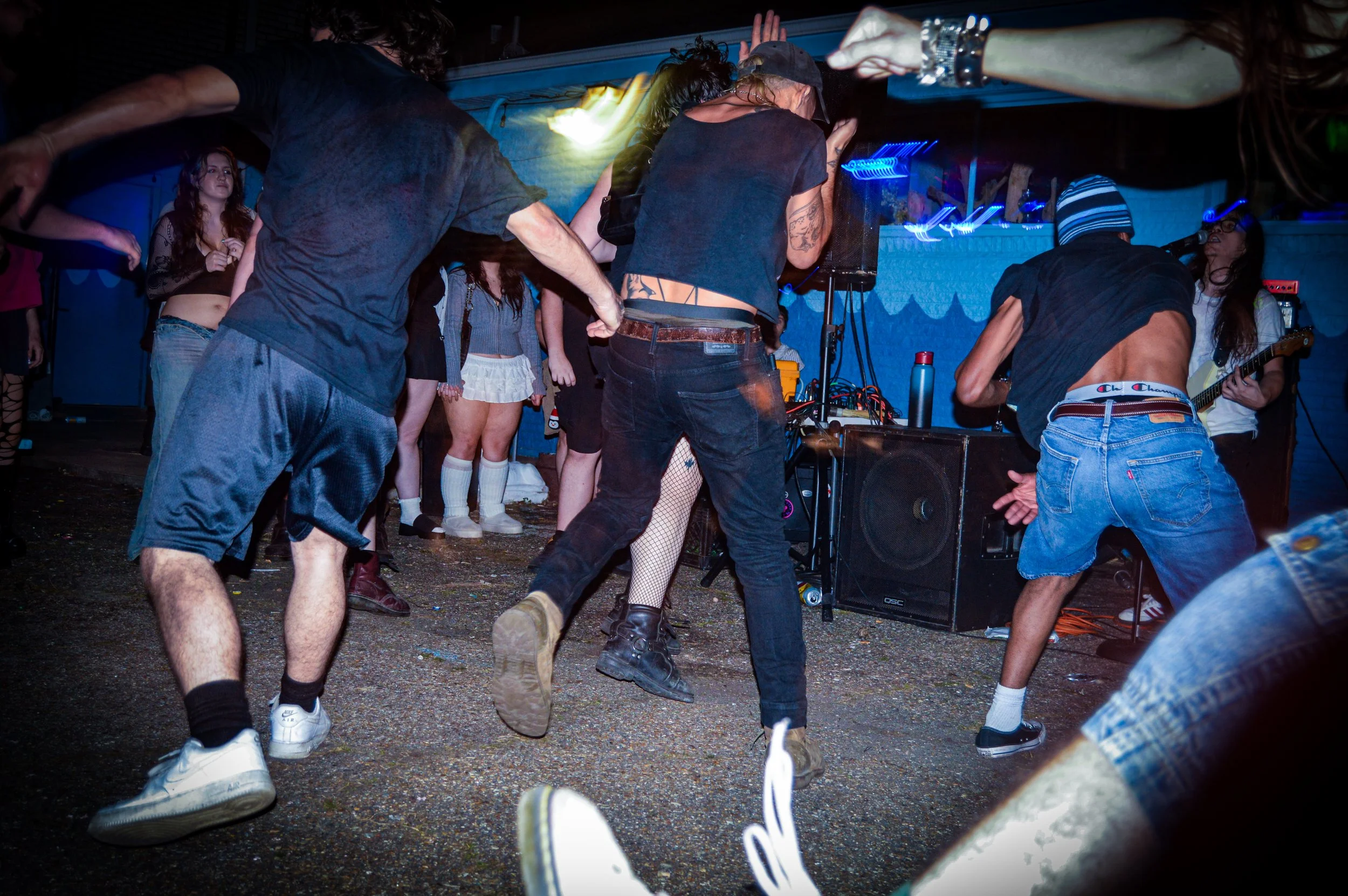 People dancing at a concert or party with a band playing in the background and colorful lights illuminating the scene.